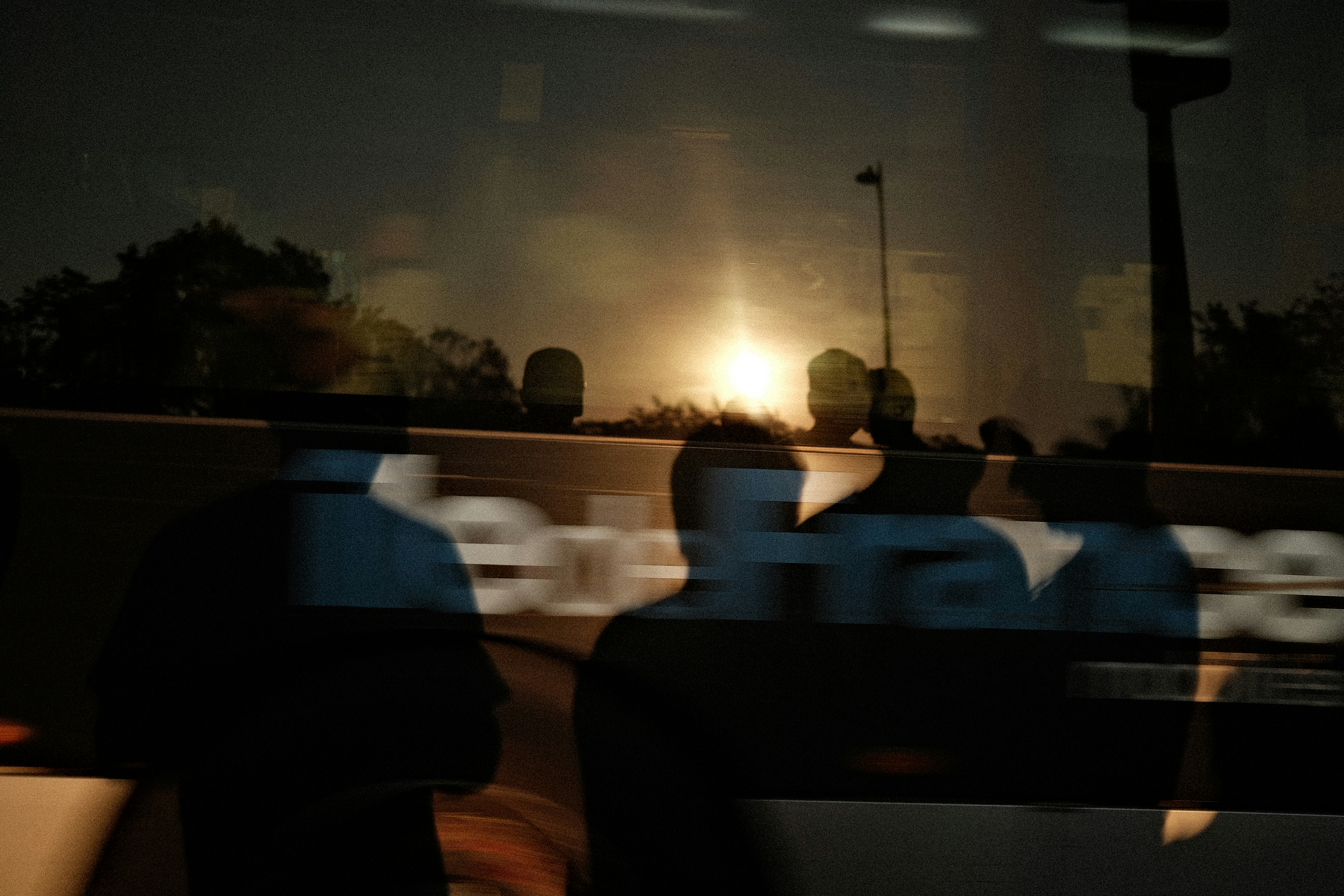 Silhouettes of people reflected in a bus window against a bright low sun