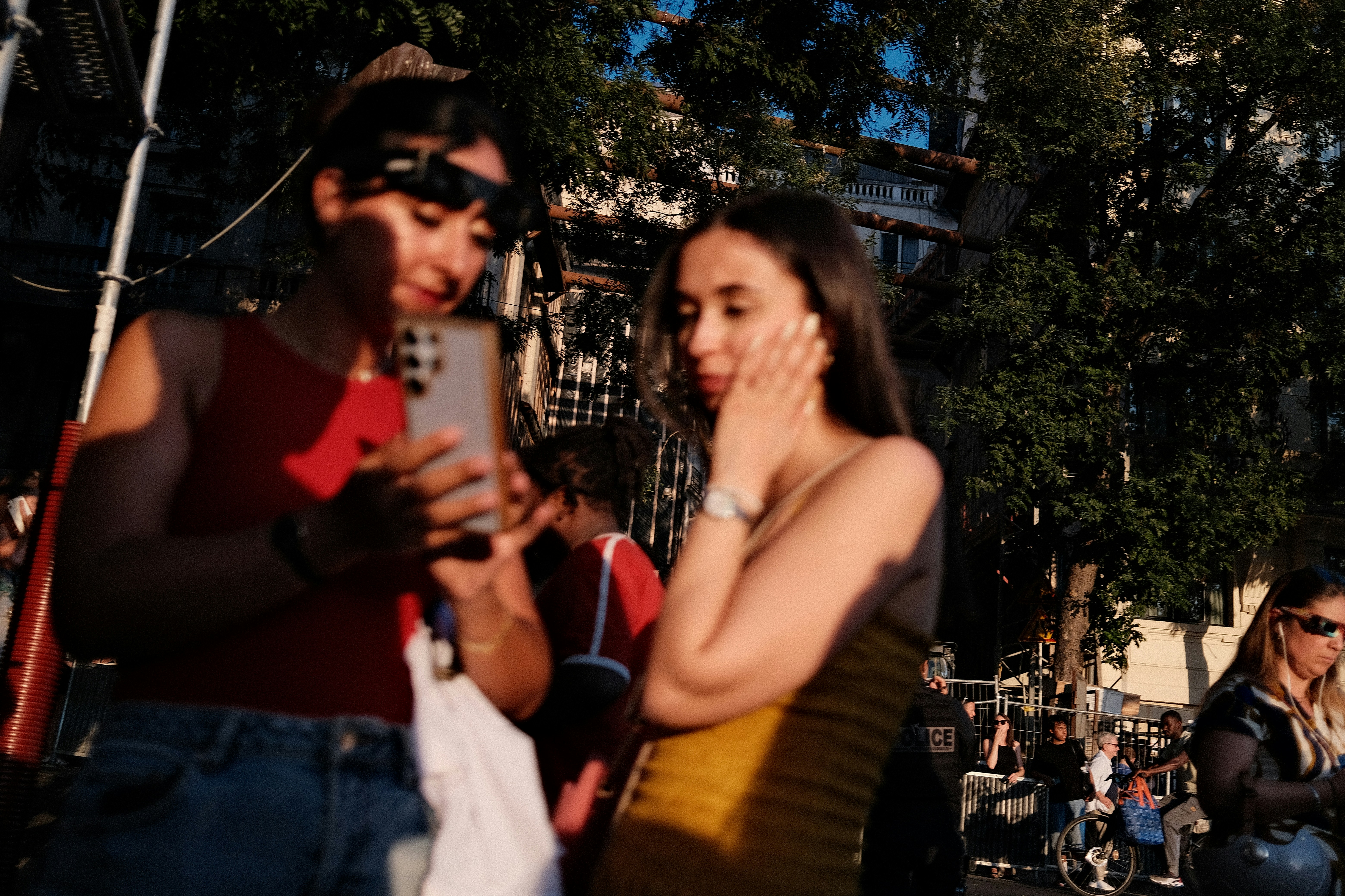 Two women in a sunlit outdoor space, one holding a smartphone