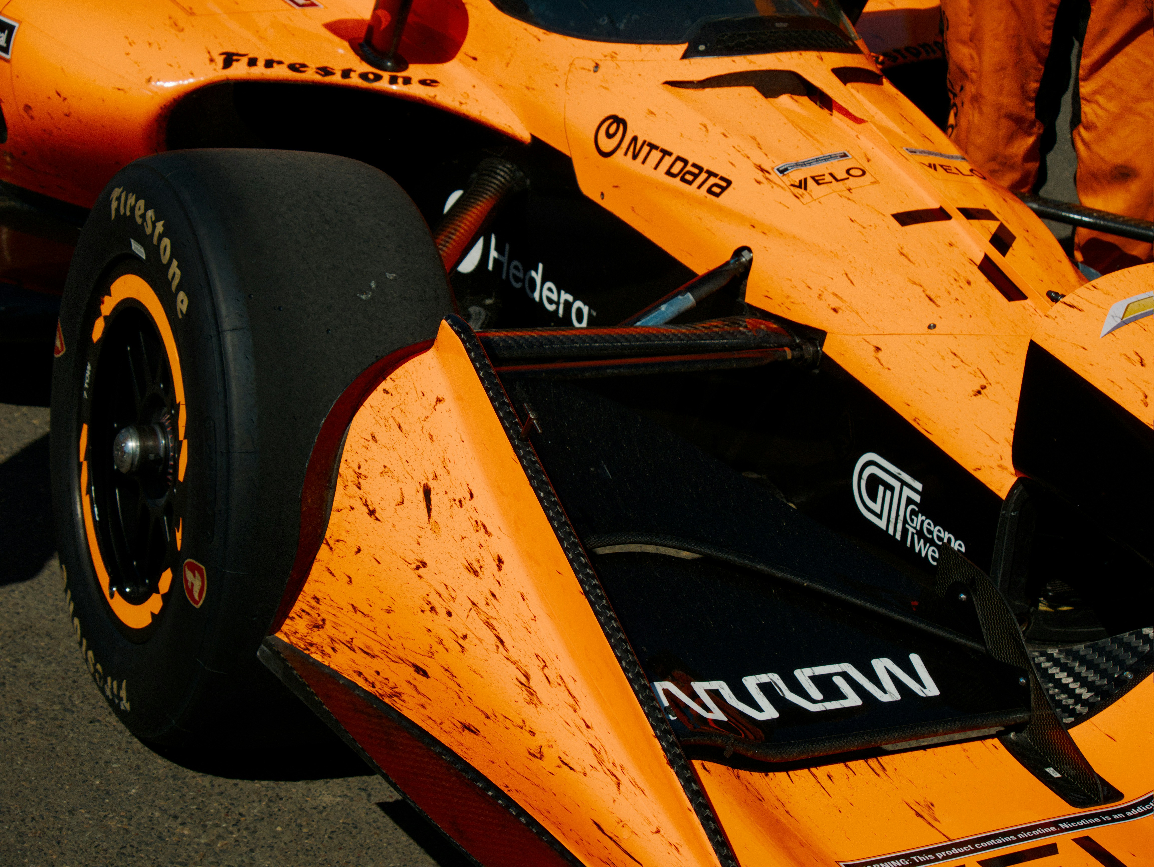 Un coche de carreras naranja salpicado de barro de IndyCar con detalles de fibra de carbono negra en un circuito