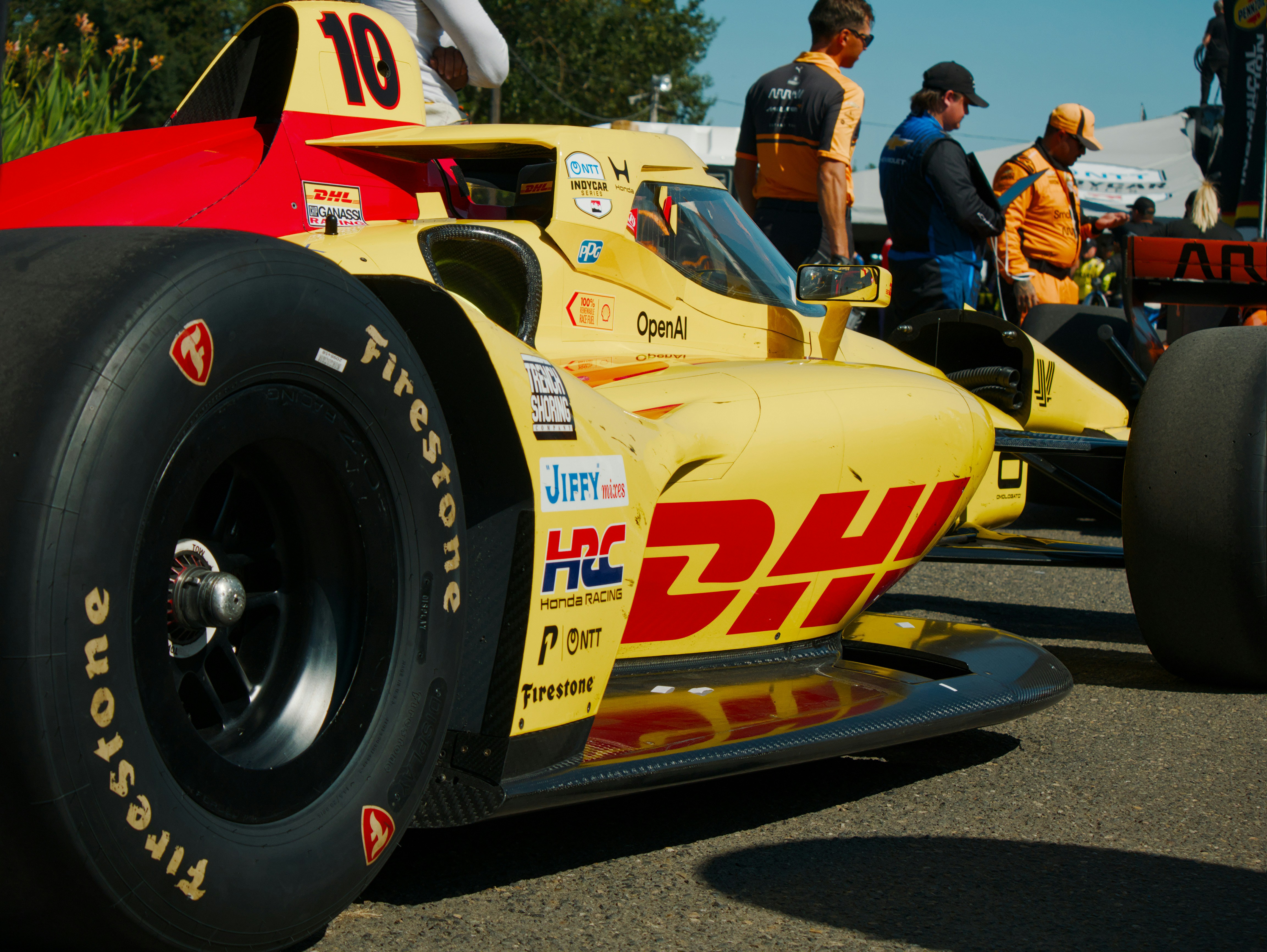 Un coche de carreras IndyCar amarillo y rojo con calcomanías de patrocinadores en un circuito