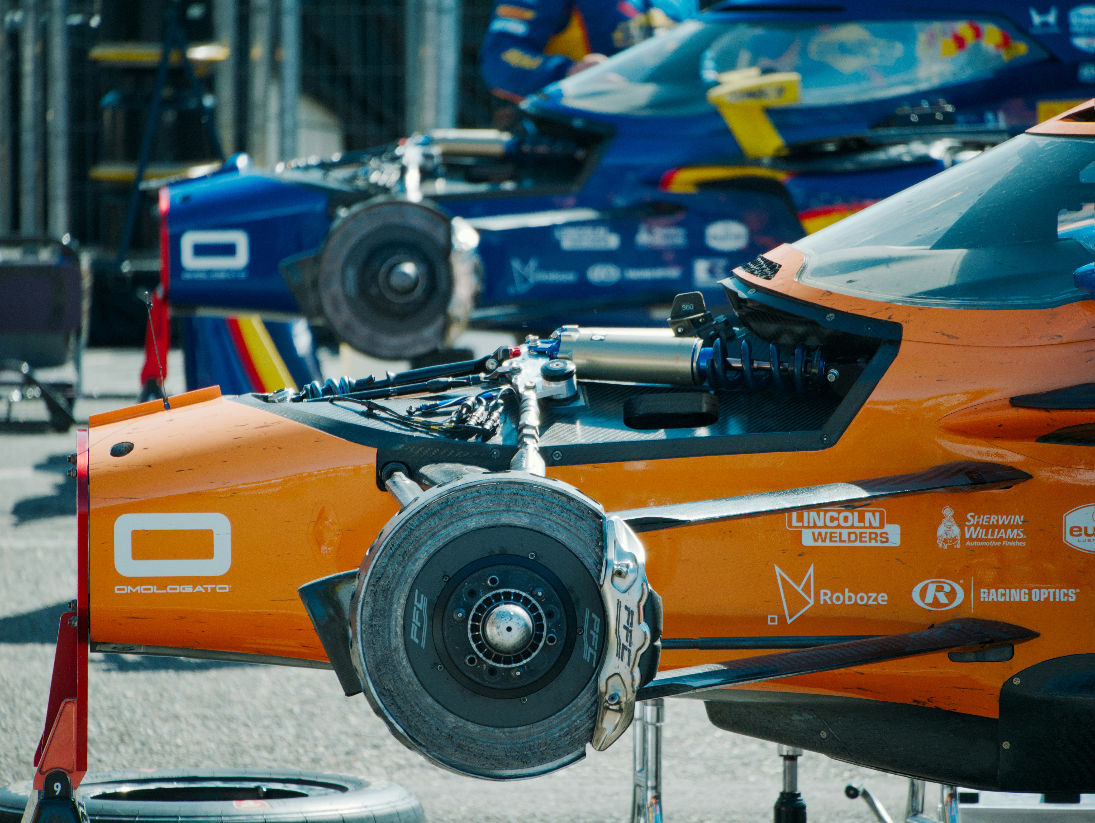 Dos coches de carreras de chasis abierto con suspensión y frenos expuestos en un pit lane