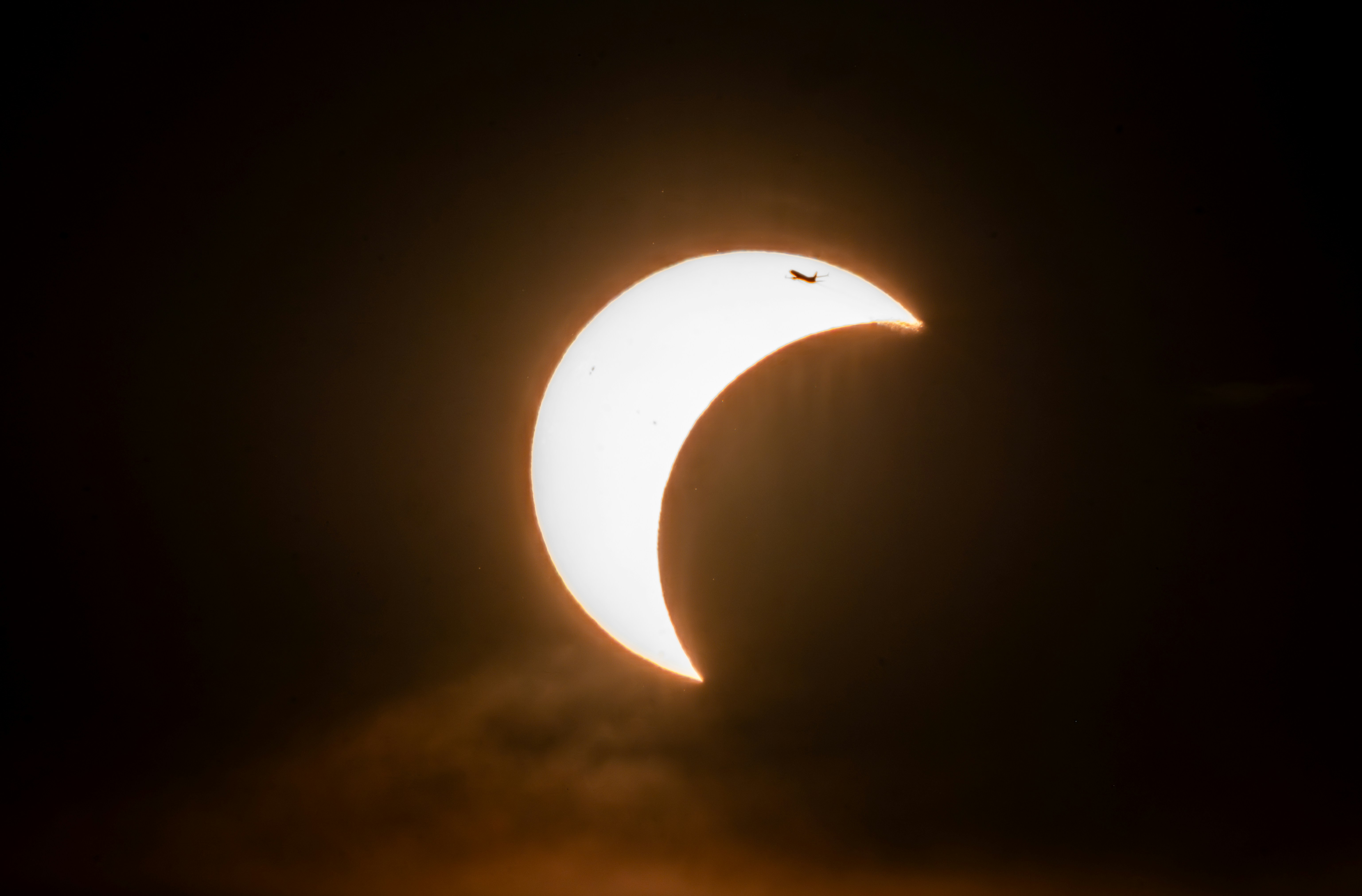 A silhouette of an airplane crossing the bright crescent of a solar eclipse.