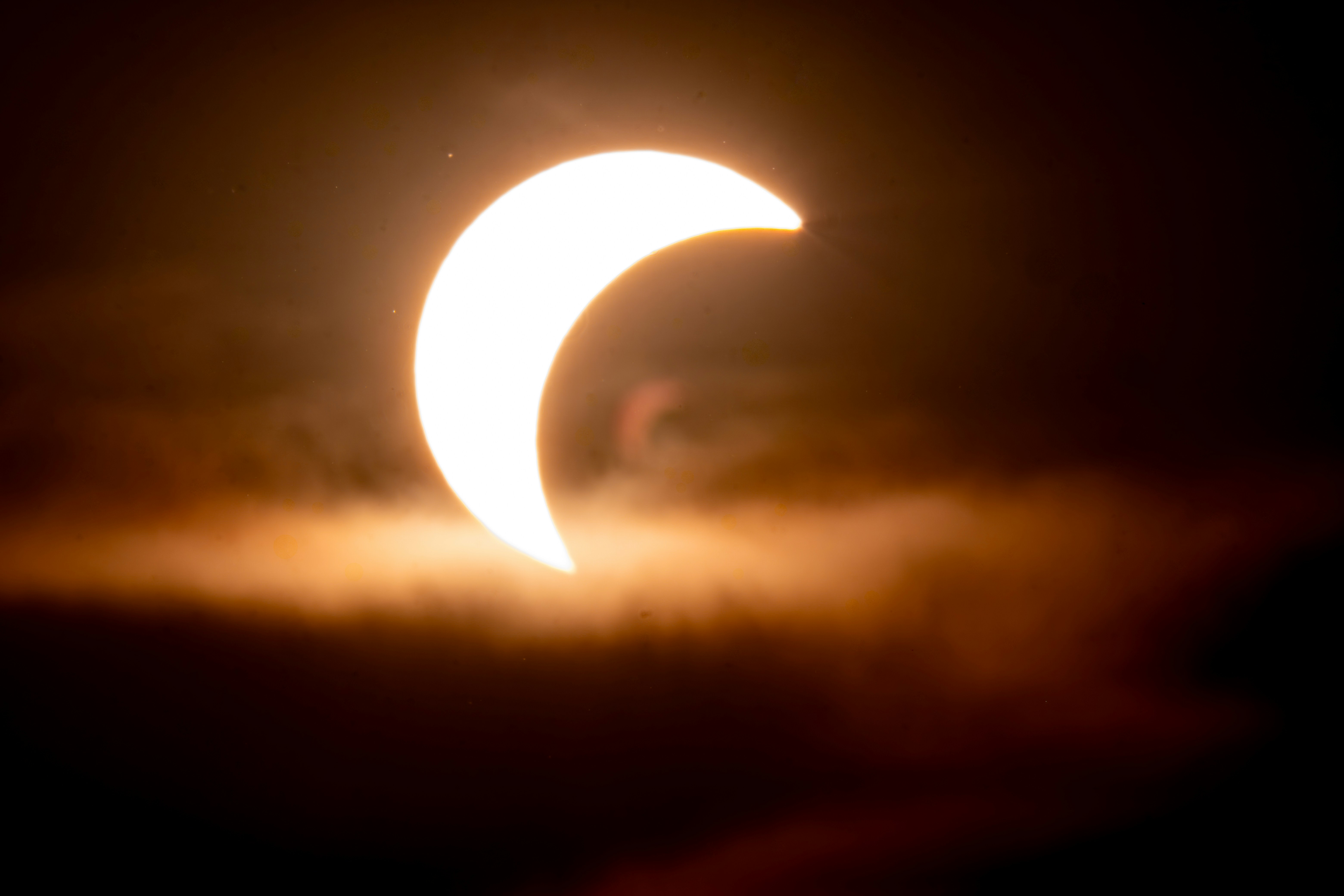 A crescent sun partially obscured by dark clouds in a dim sky.