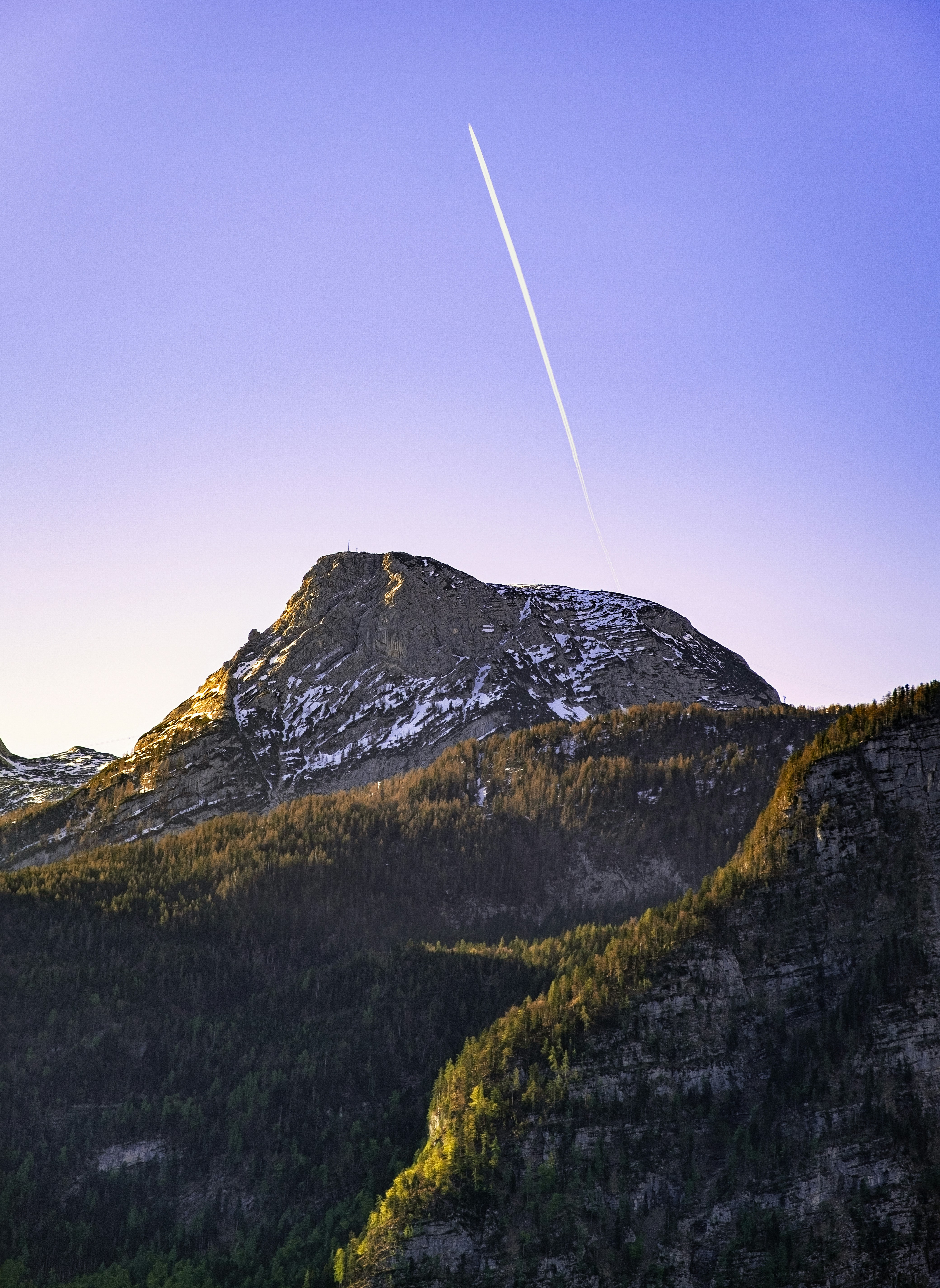 A snow-capped mountain peak with a contrail in a clear blue sky