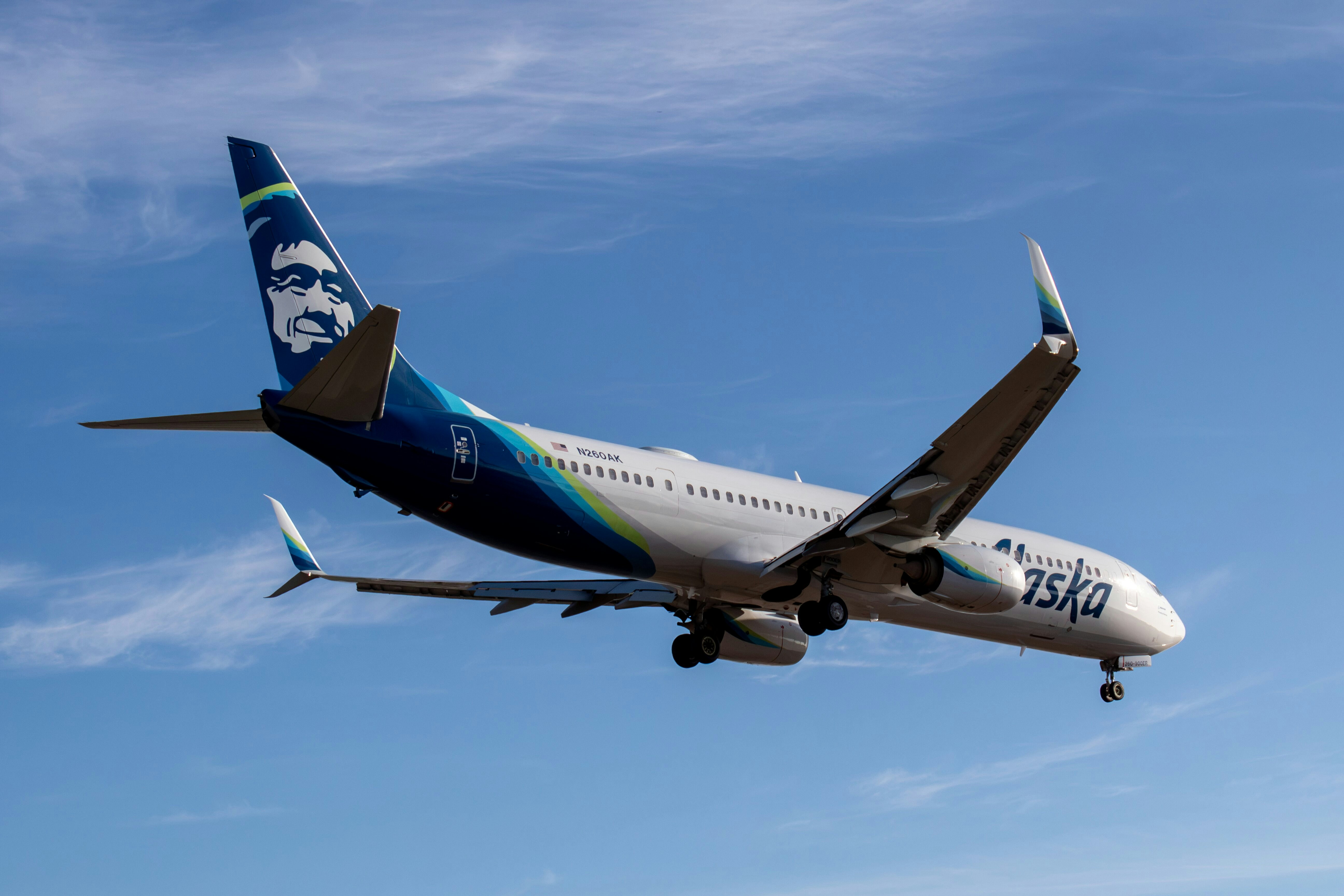 An Alaska Airlines passenger jet descending through a clear blue sky