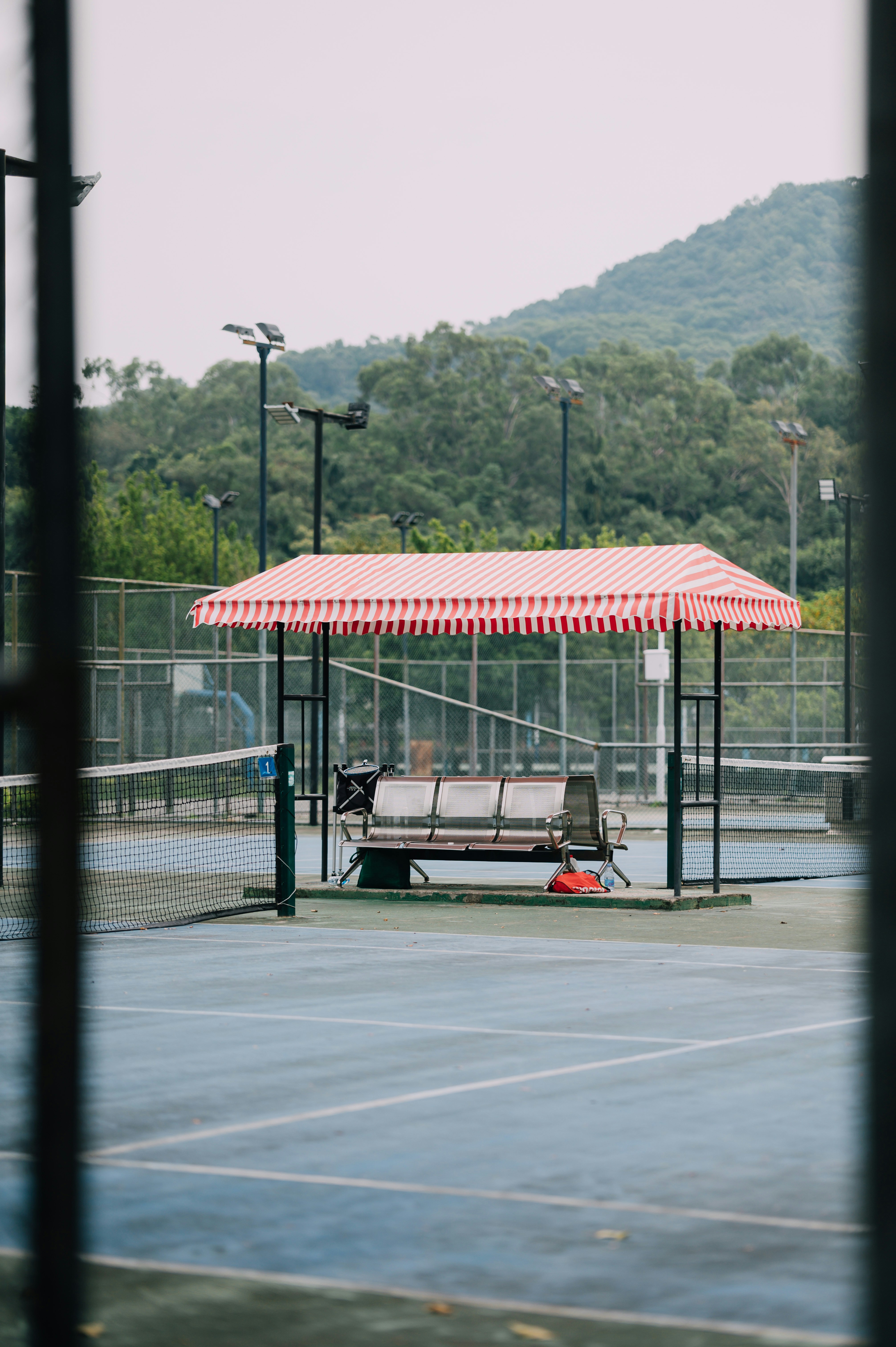 A metal bench under a red and white striped canopy on a tennis court
