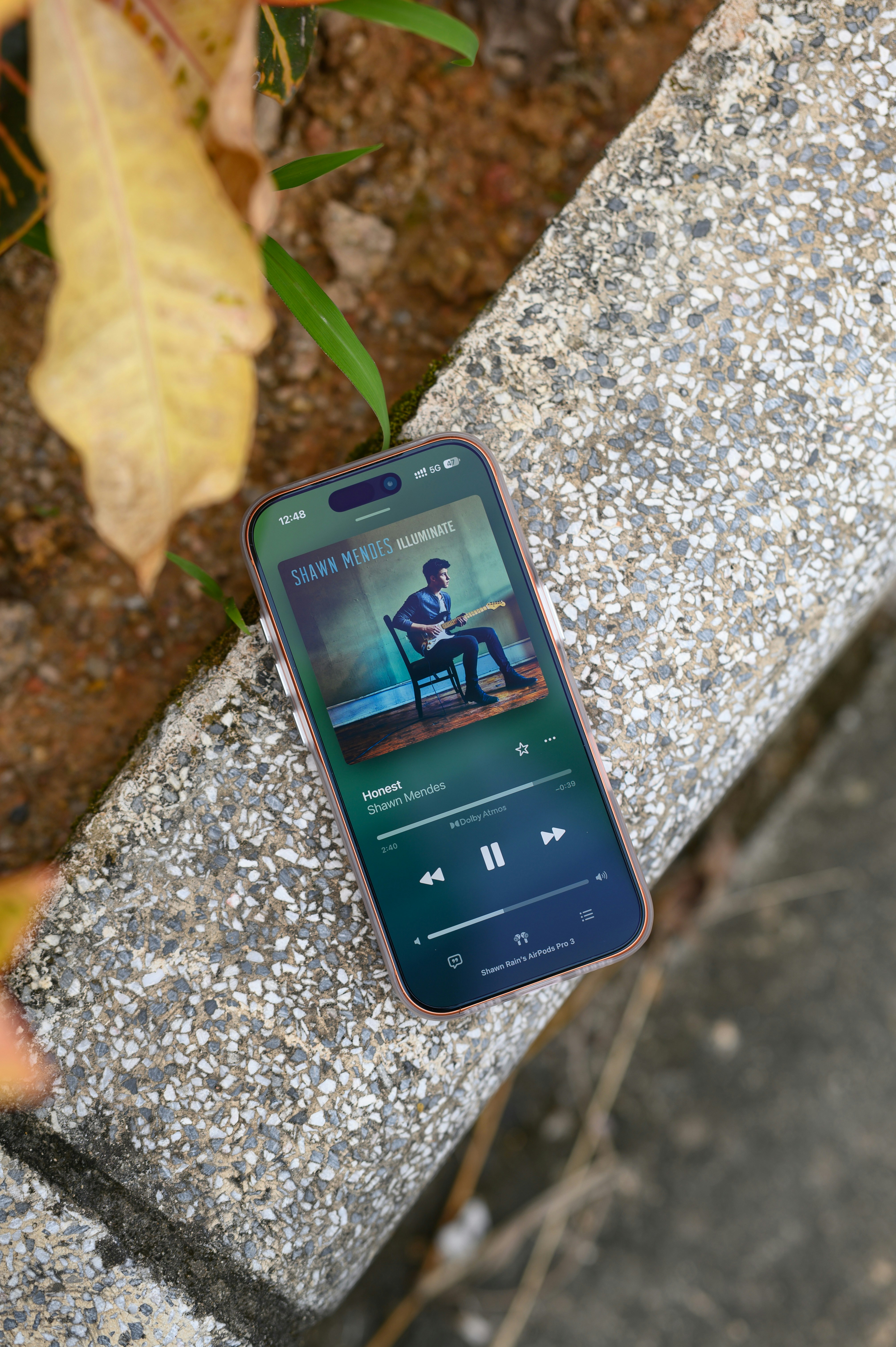 A smartphone displaying a music player interface on a speckled stone ledge