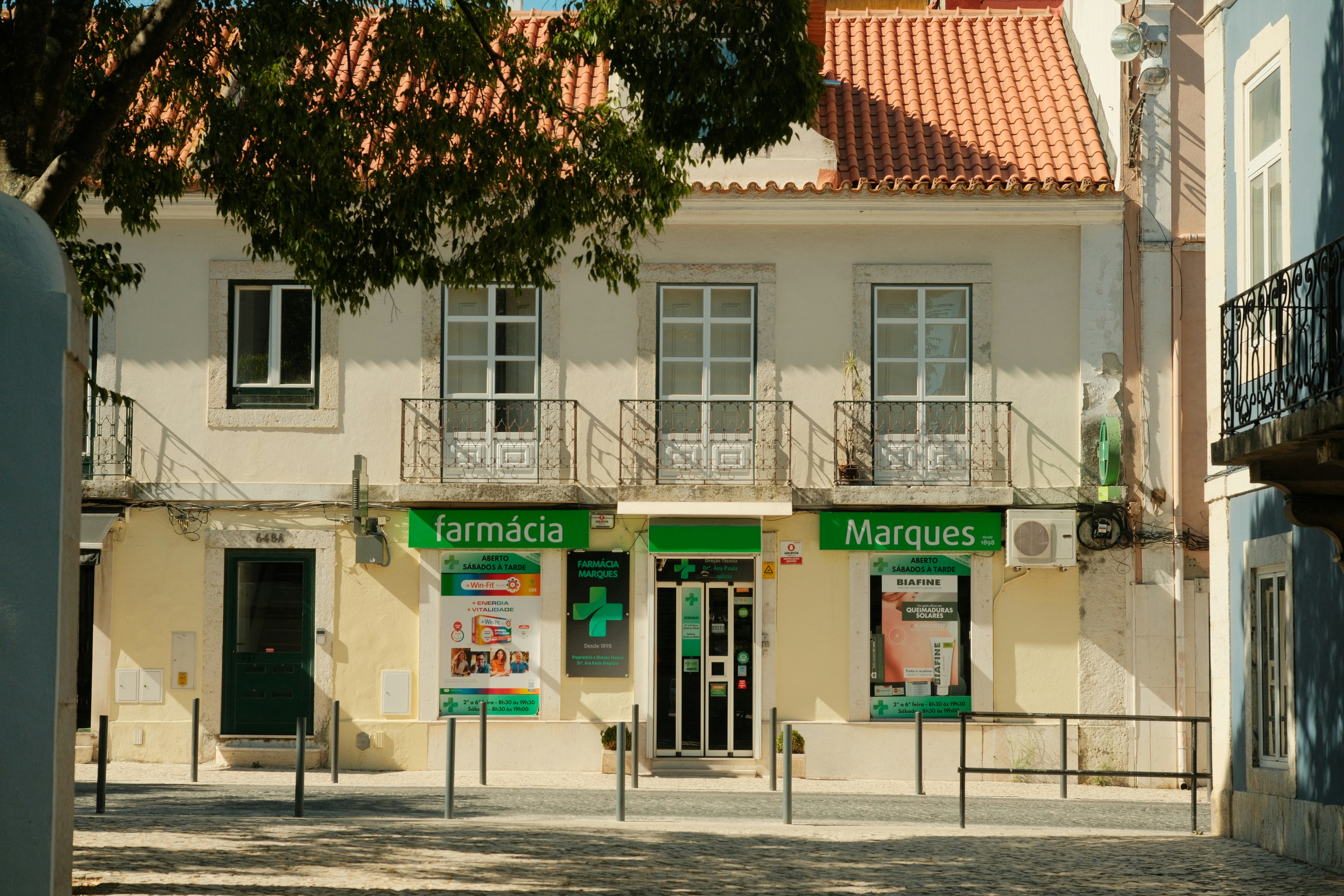 A pharmacy with green signage and a tiled roof on a sunny street