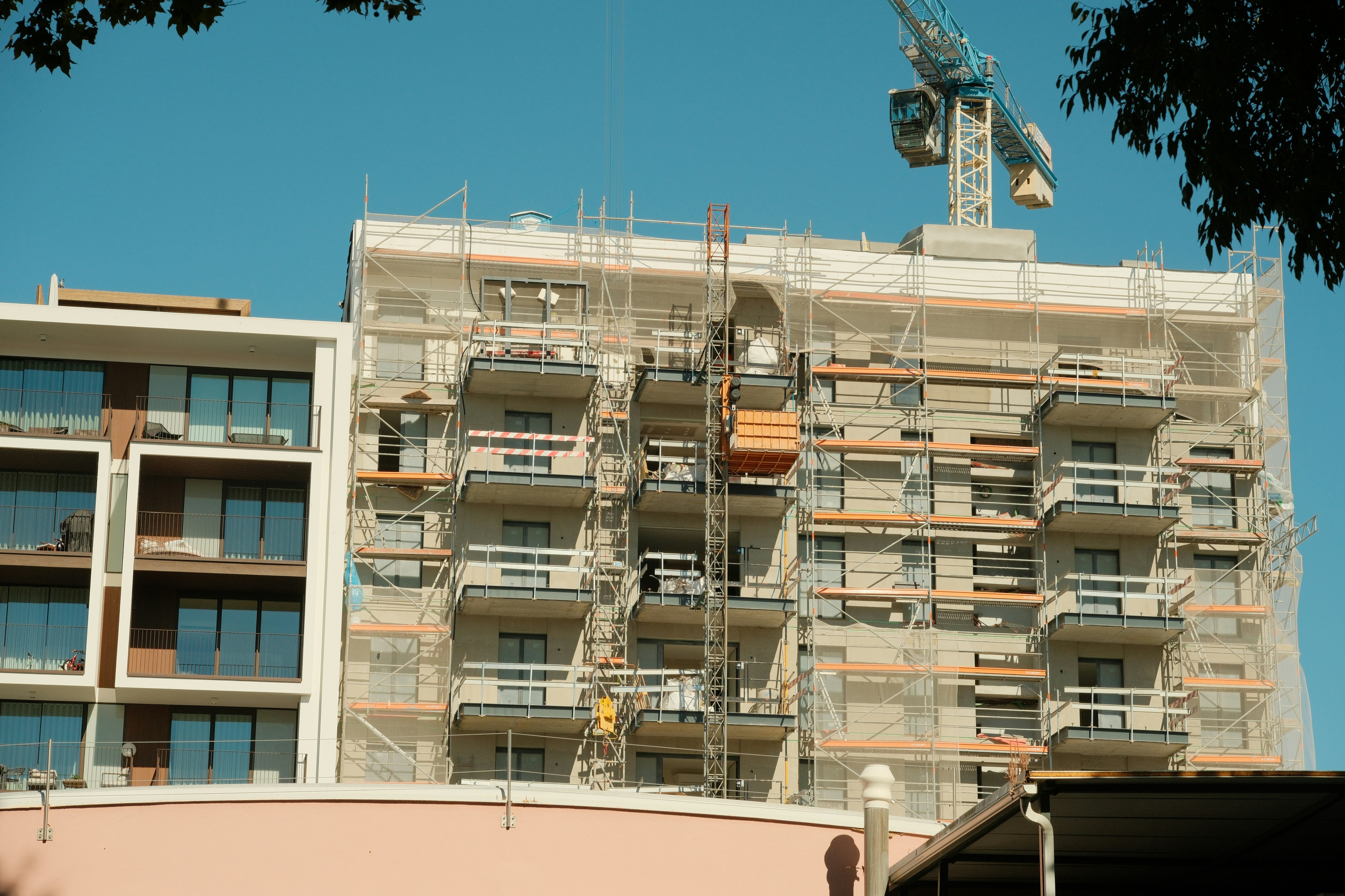 A multi-story apartment building under construction with scaffolding and a blue crane