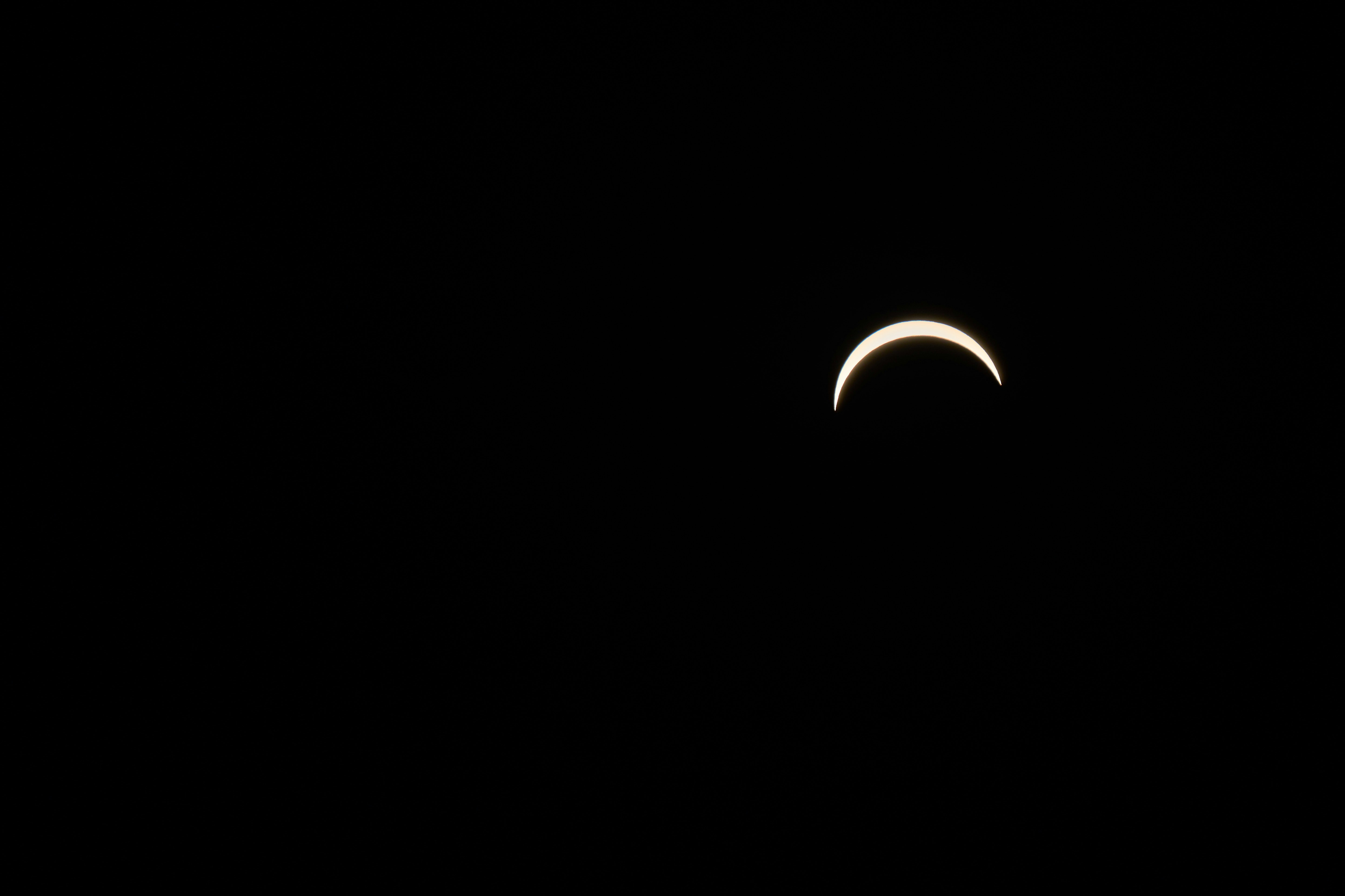 A thin crescent of the sun glowing against a deep black sky.
