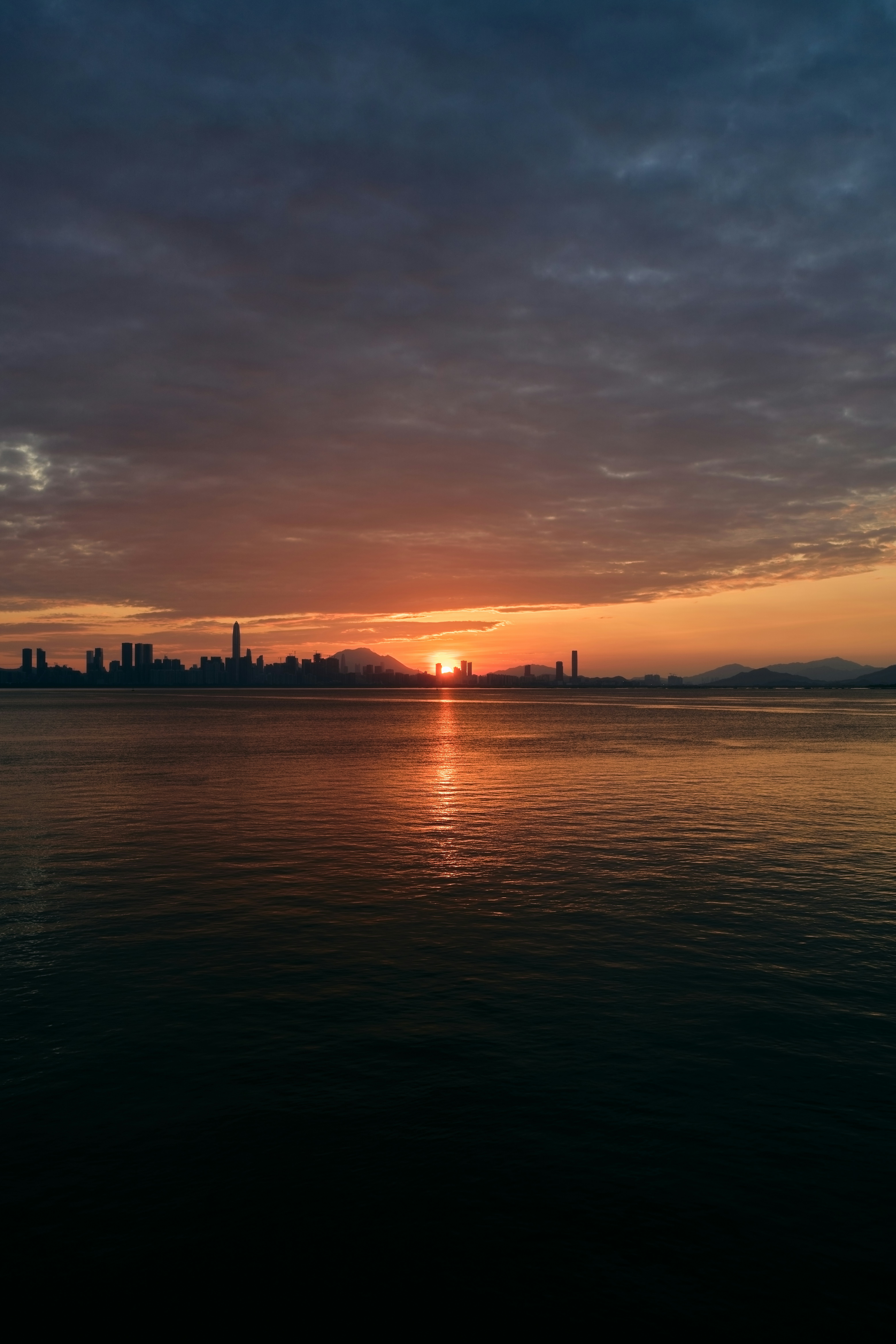A city skyline silhouette across the water under a warm orange sky.