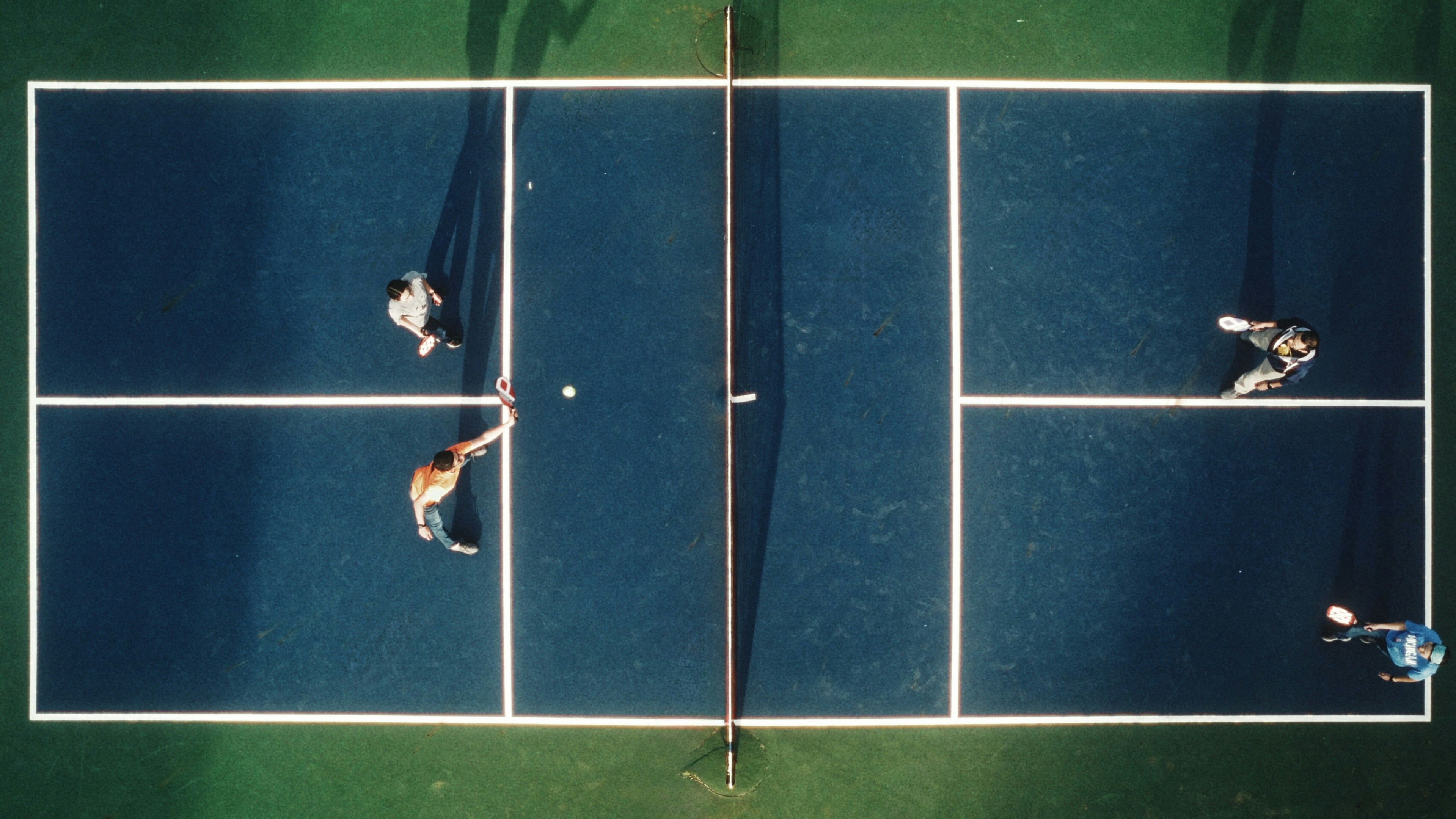 Una vista aerea di quattro persone che giocano a pickleball su un campo blu.