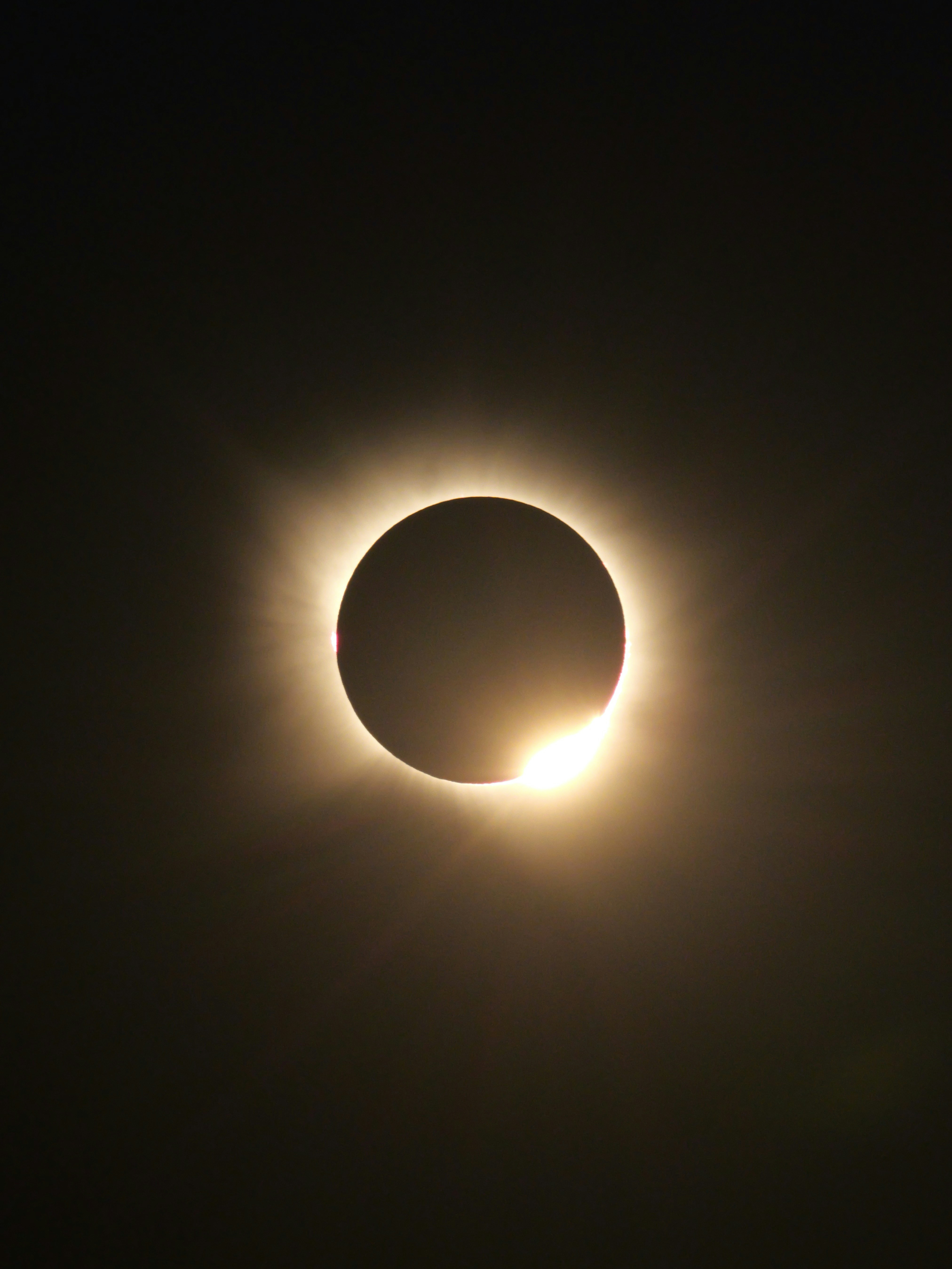 A total solar eclipse with a bright diamond ring effect in the dark sky.