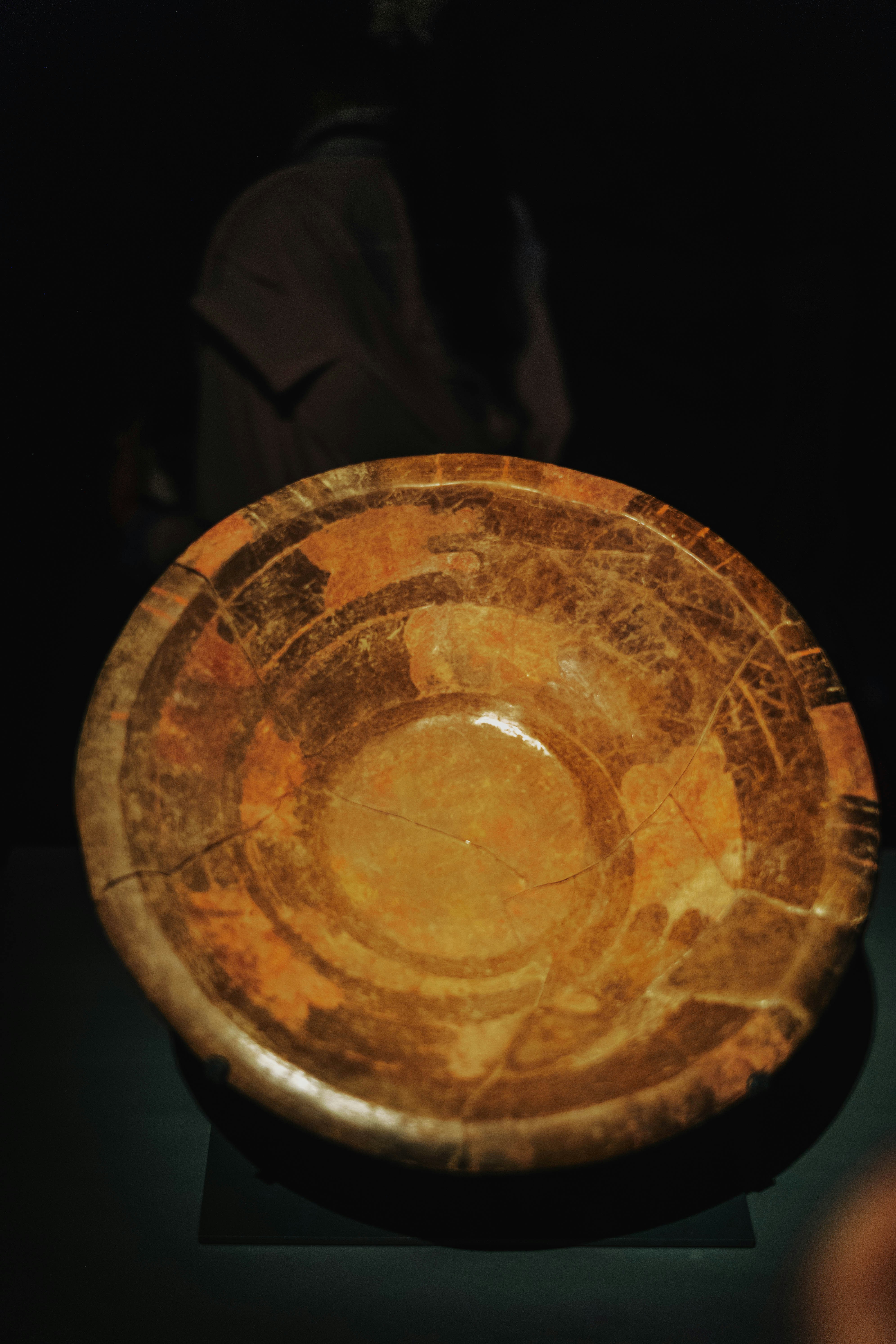 An ancient cracked ceramic bowl with a mottled orange and brown surface.