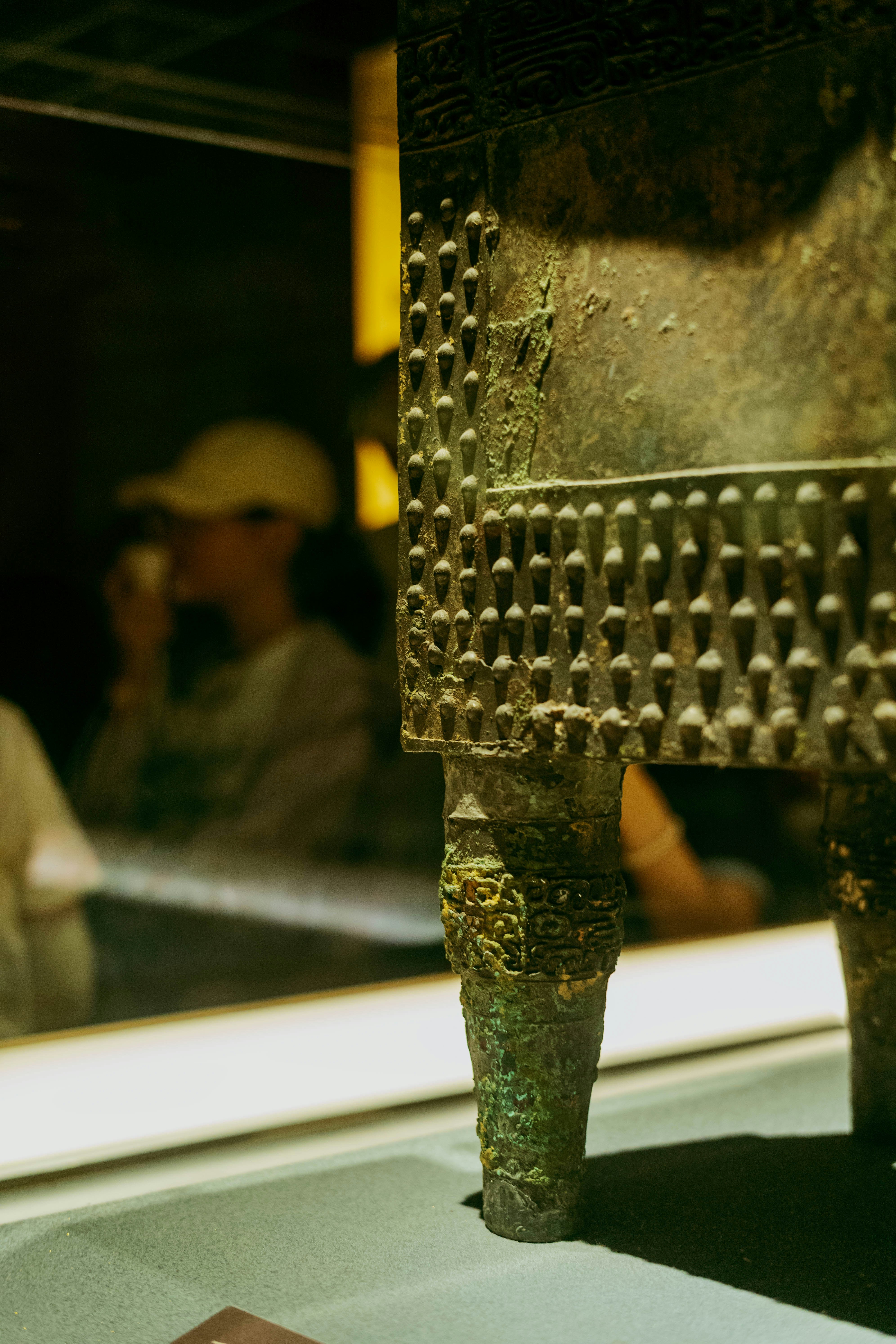 An ancient bronze vessel with textured studs on a display stand in a museum.