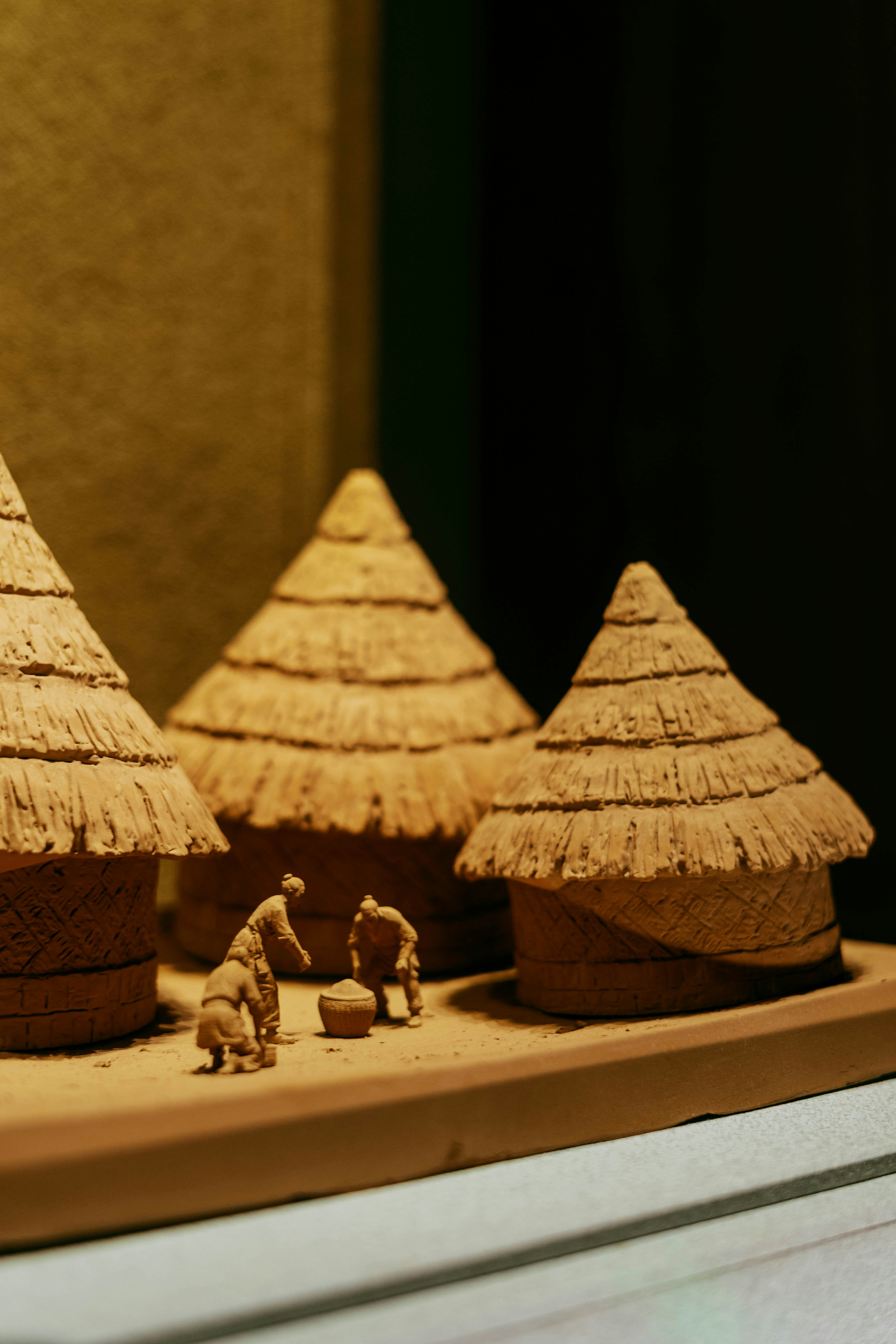 Clay model of three thatched huts with three small figures in a village.