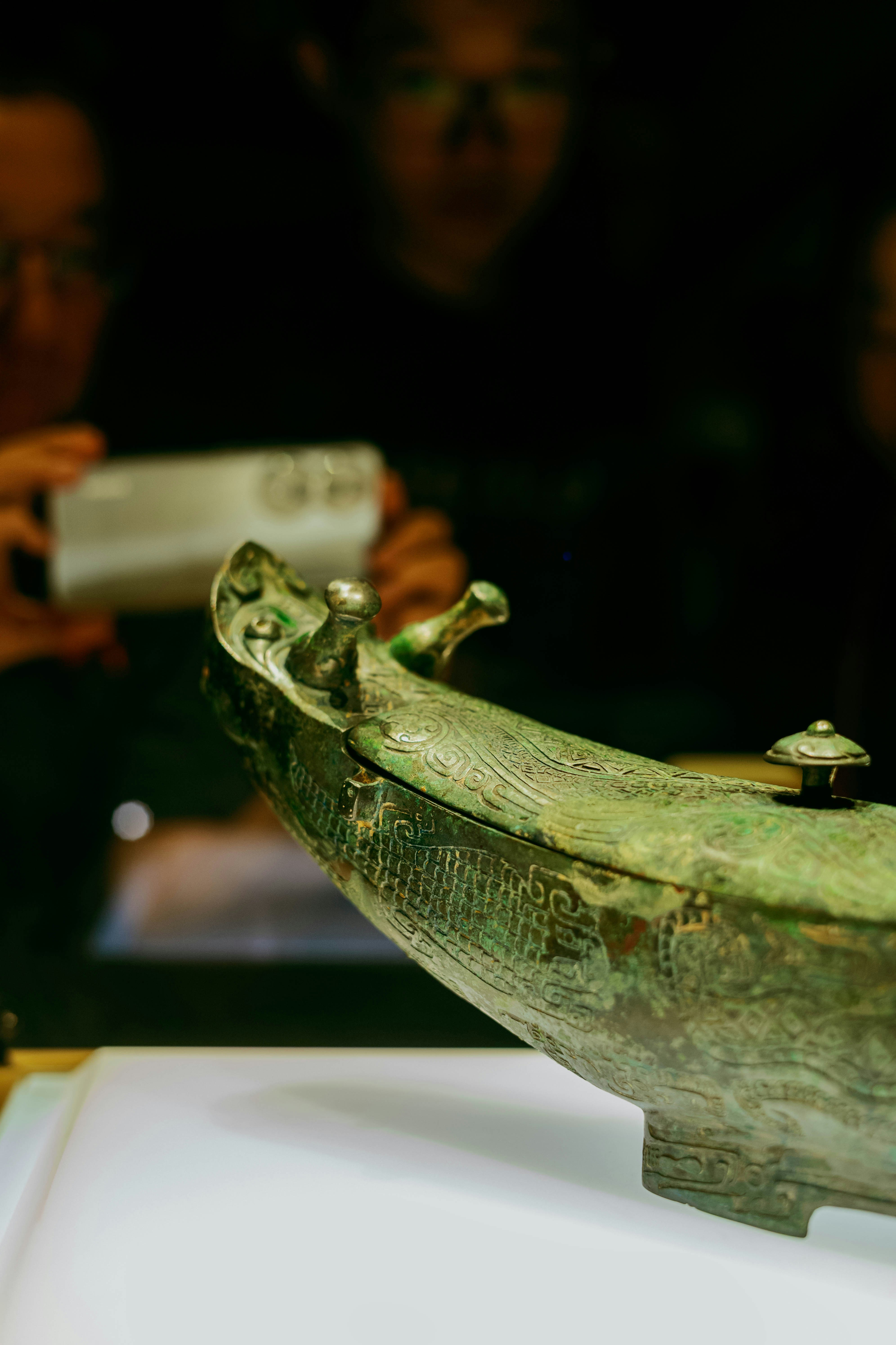 An ancient bronze vessel with intricate carvings on a white display surface.