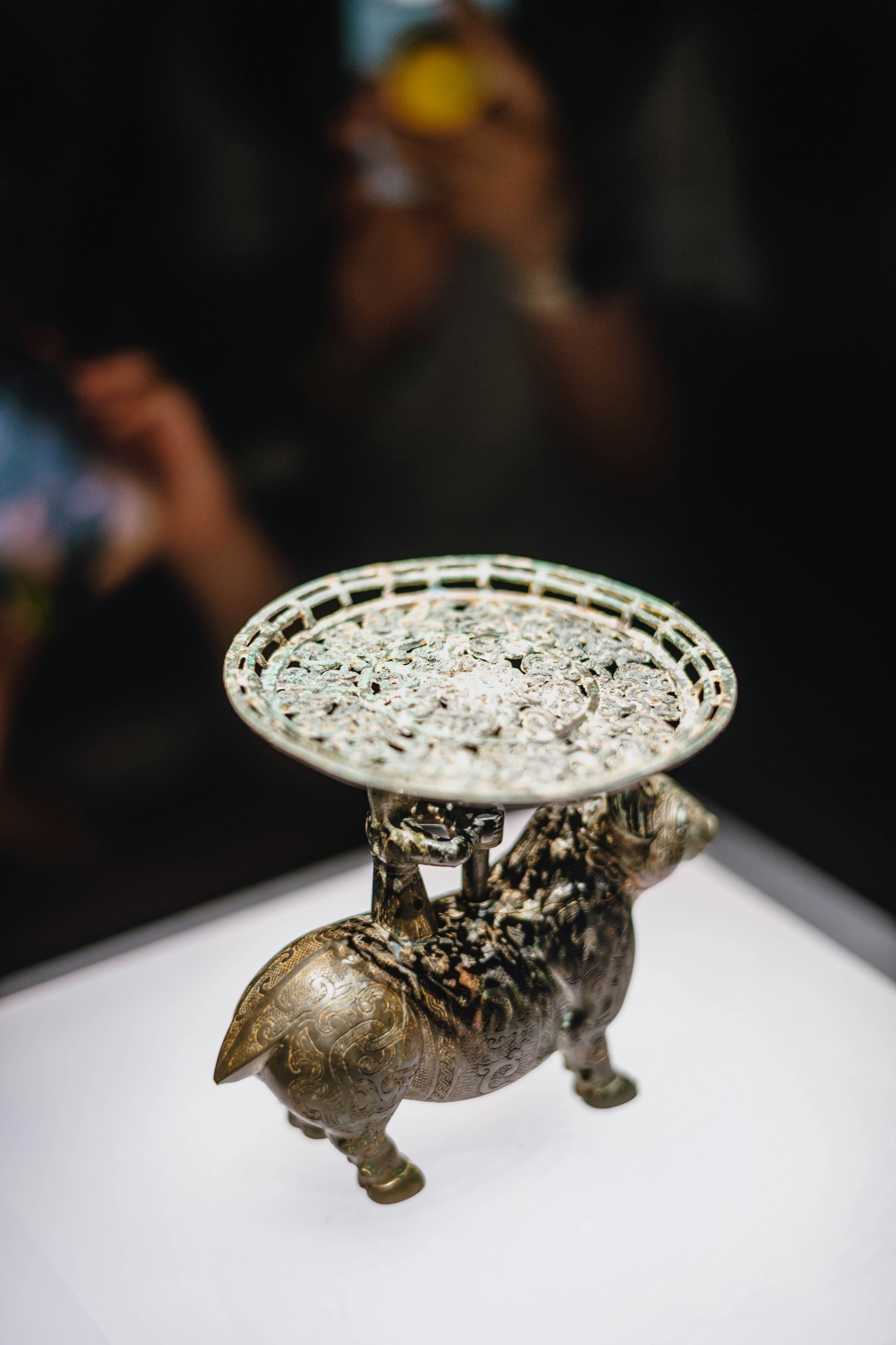 An ornate bronze animal figurine supporting a circular tray on a white display stand.