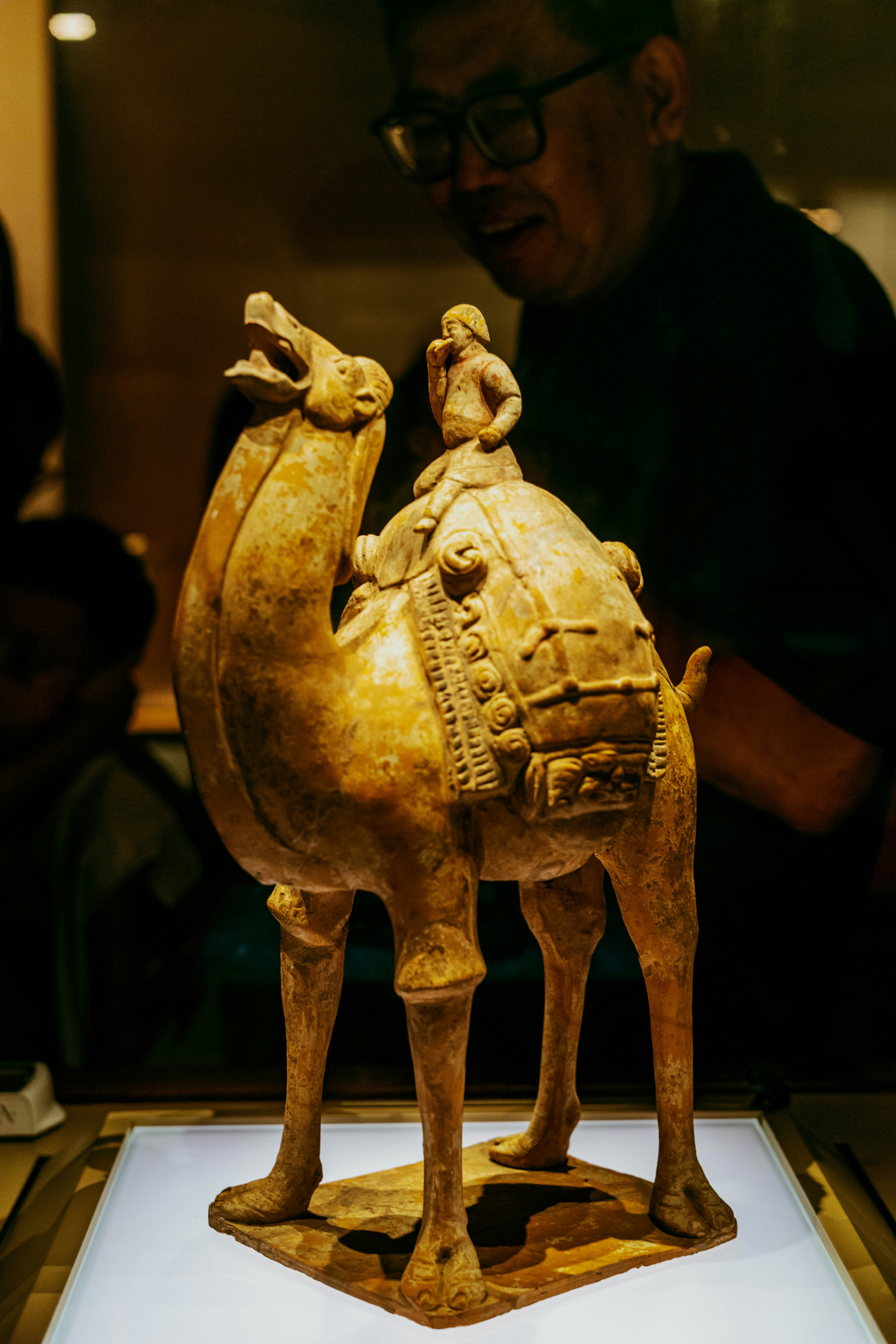 A terracotta camel figurine with a rider on its back in a museum display.