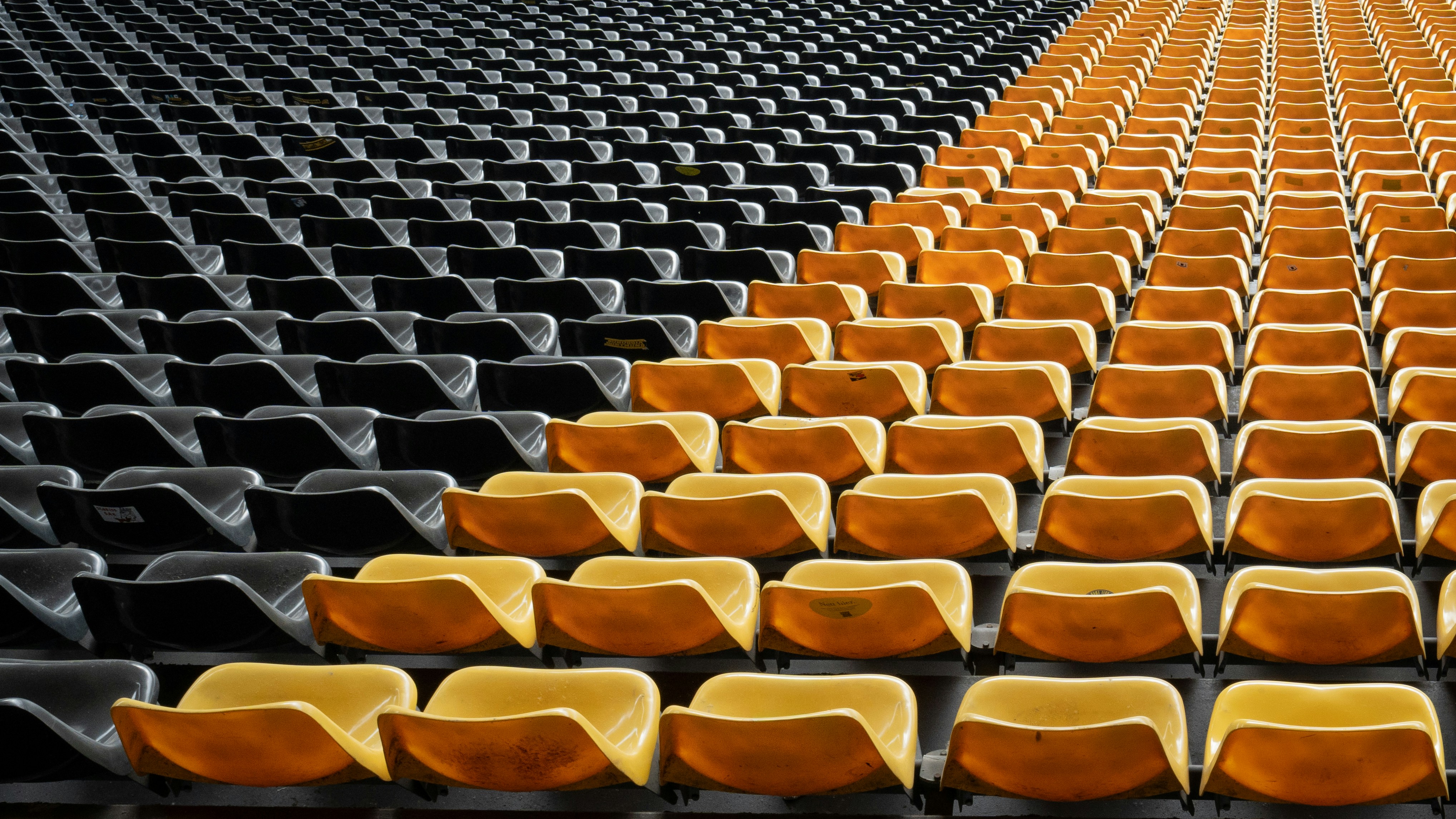Barisan kursi stadion hitam dan kuning kosong disusun dalam pola diagonal.