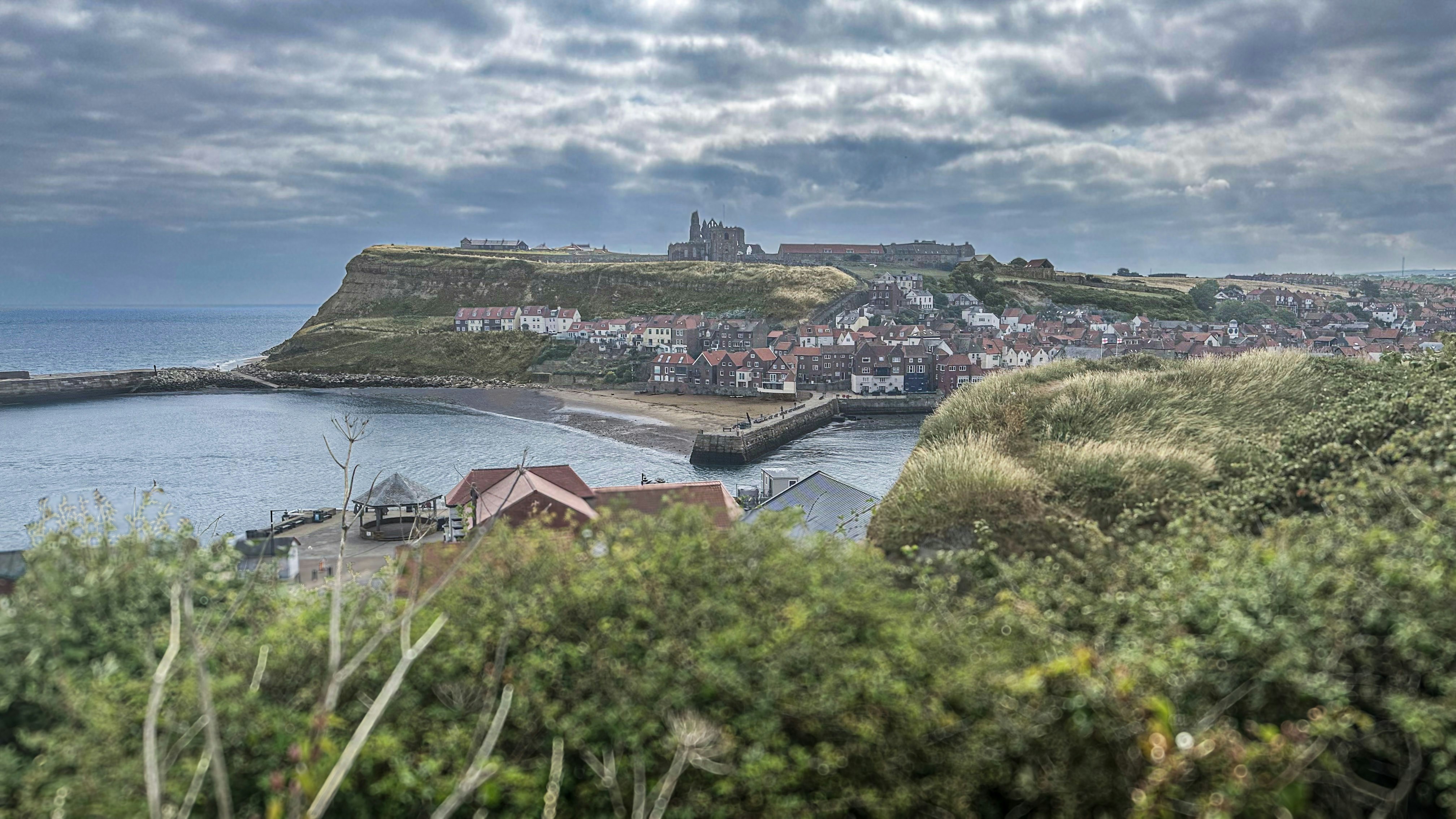 Whitby Abbey ruins overlooking the coastal town and harbor under a cloudy sky