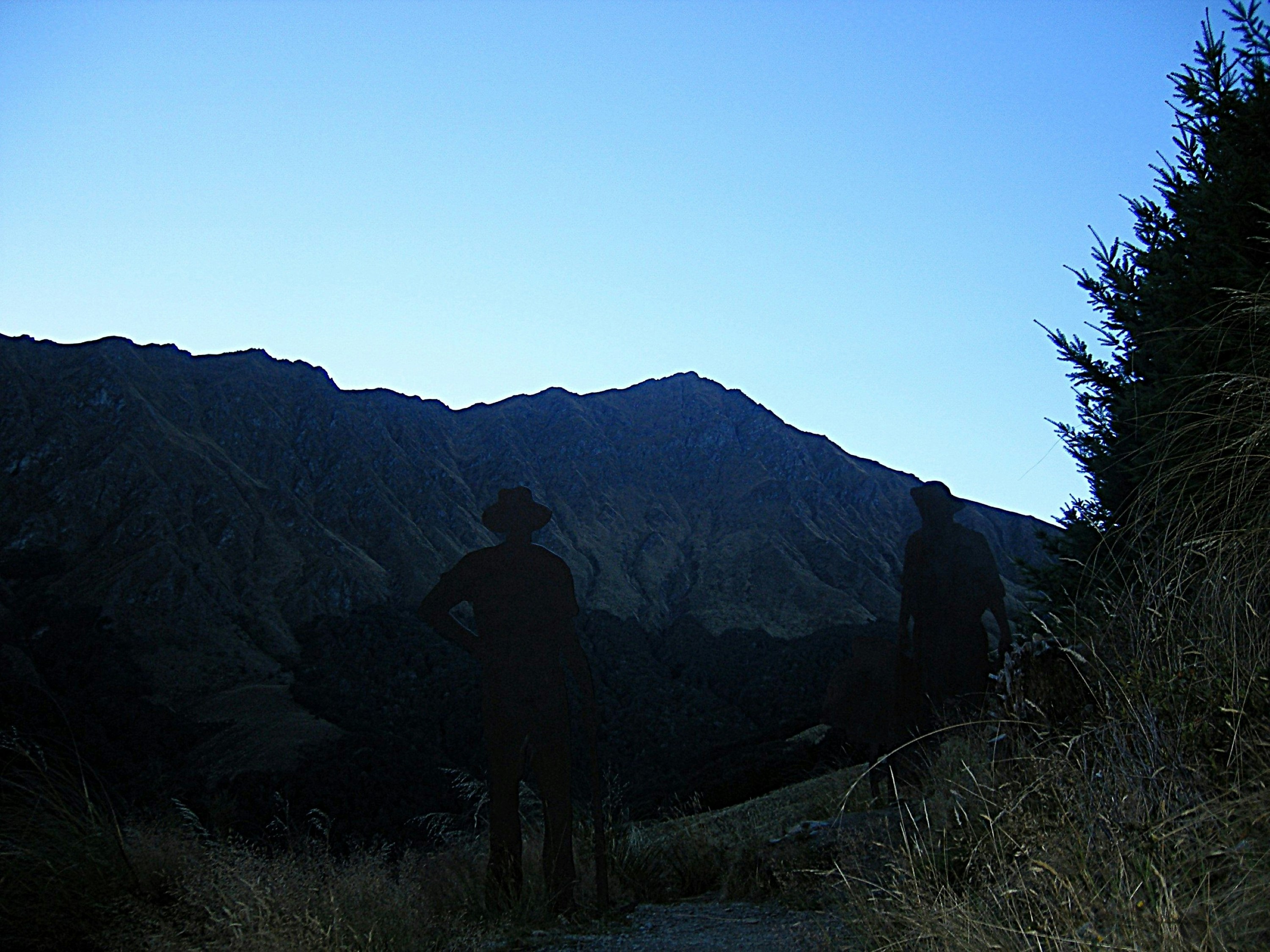 Two people in silhouette on a mountain trail against a clear blue sky