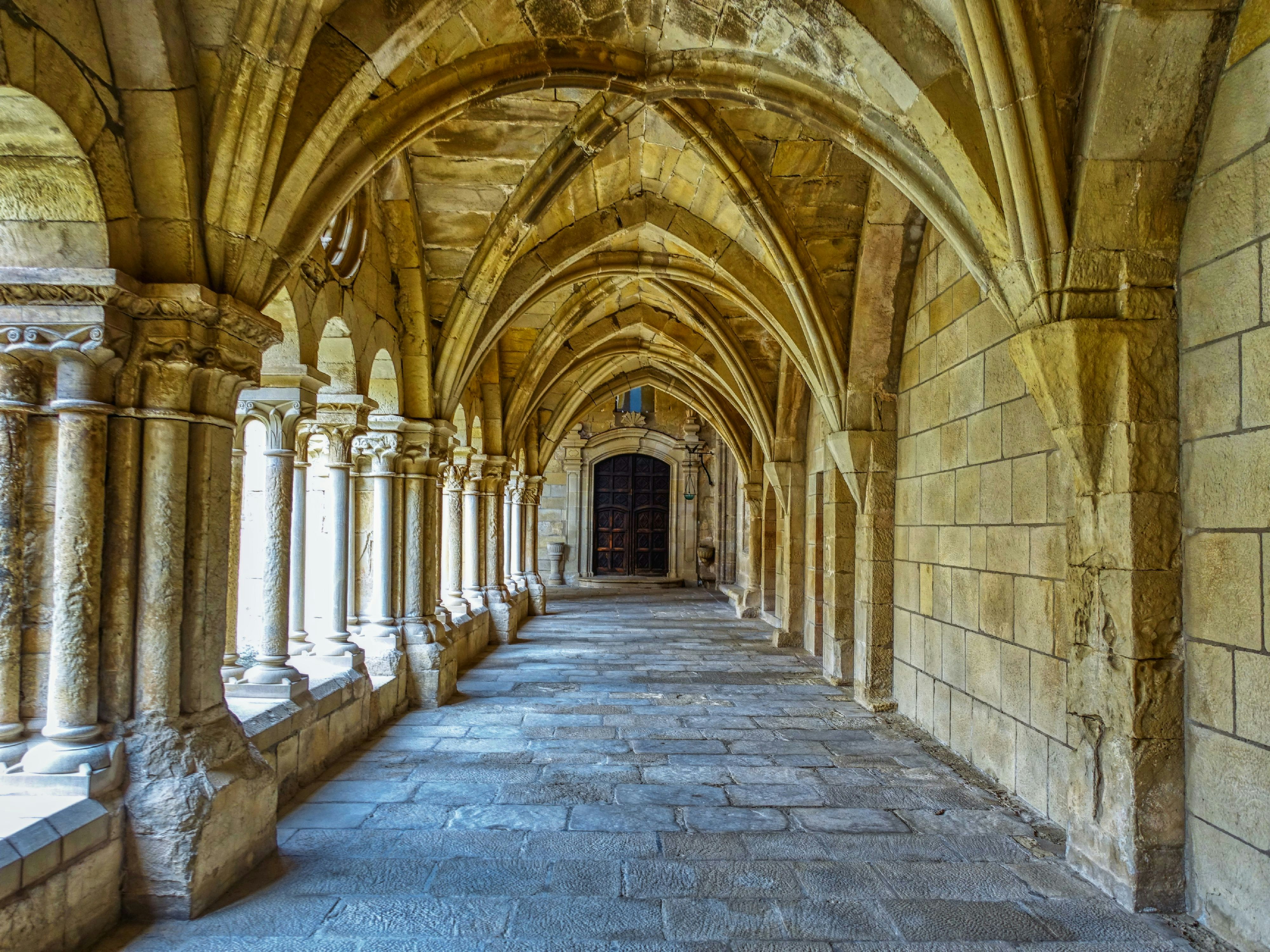 Um claustro de pedra com tetos abobadados e colunas alinhadas por uma passarela pavimentada