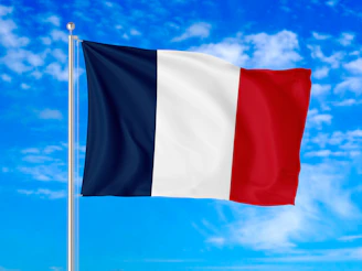 The flag of France waving on a metal pole against a blue sky