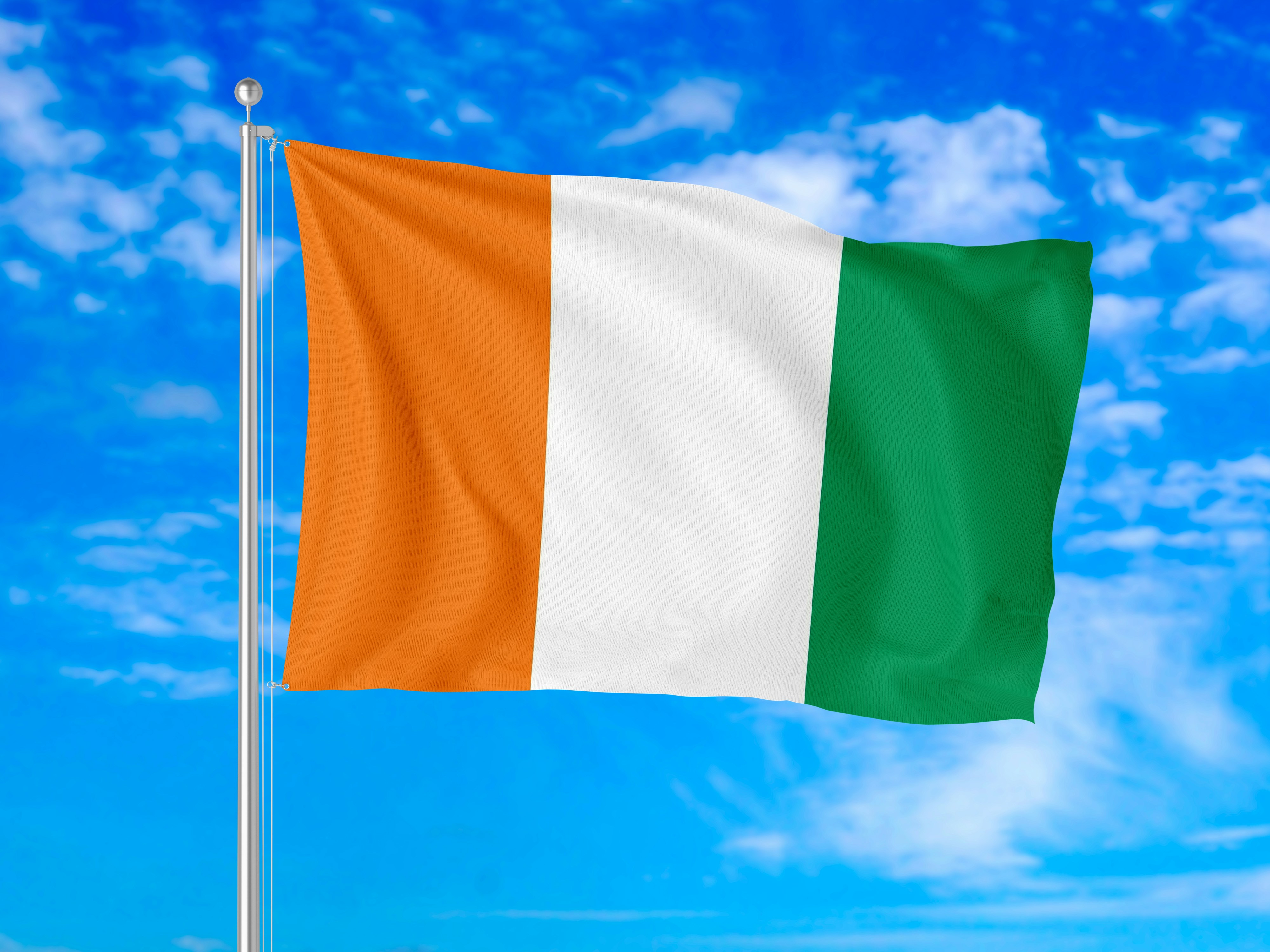 The flag of Ivory Coast waving on a pole against a blue sky