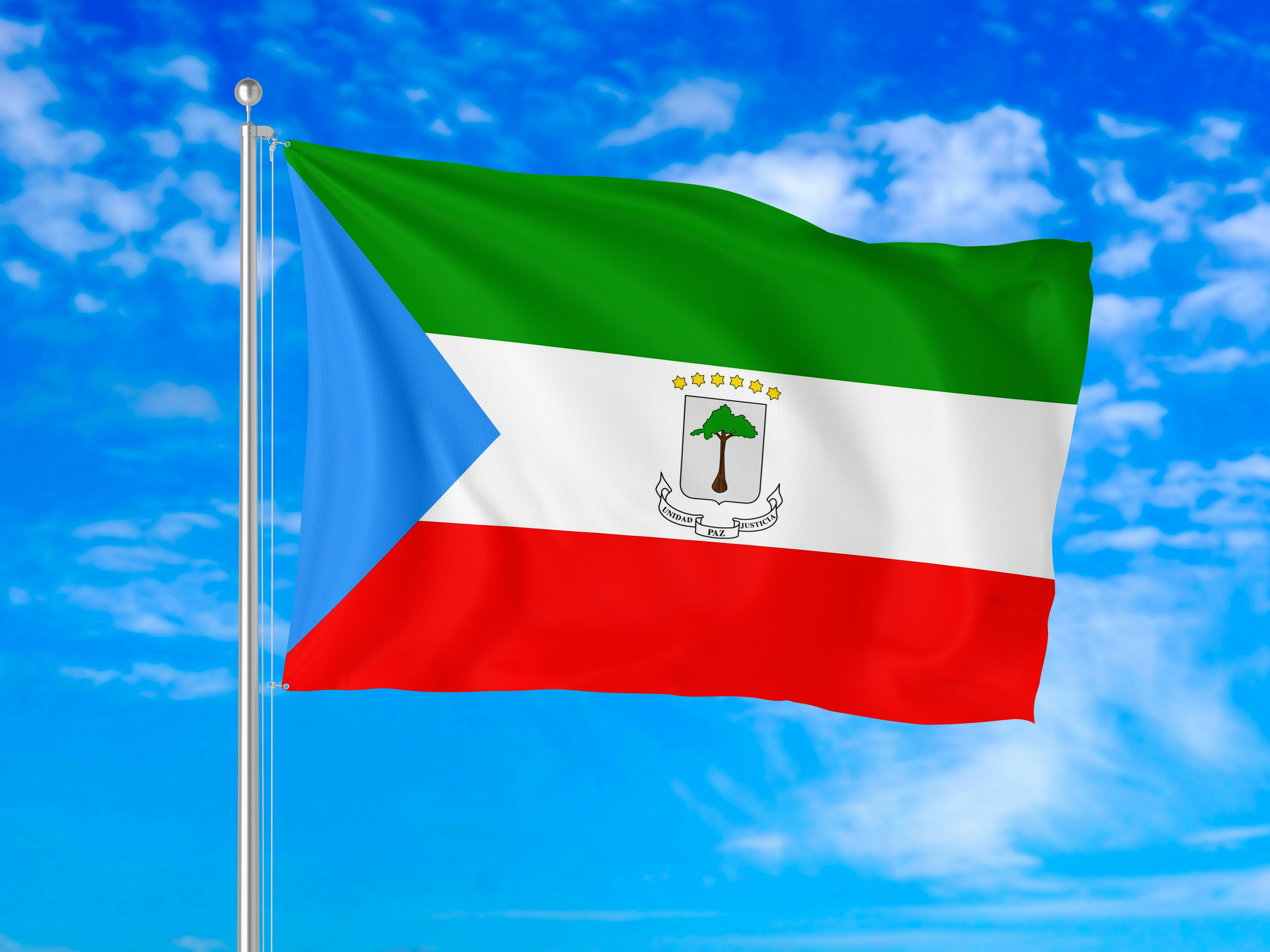 The flag of Equatorial Guinea waving on a pole against a blue sky