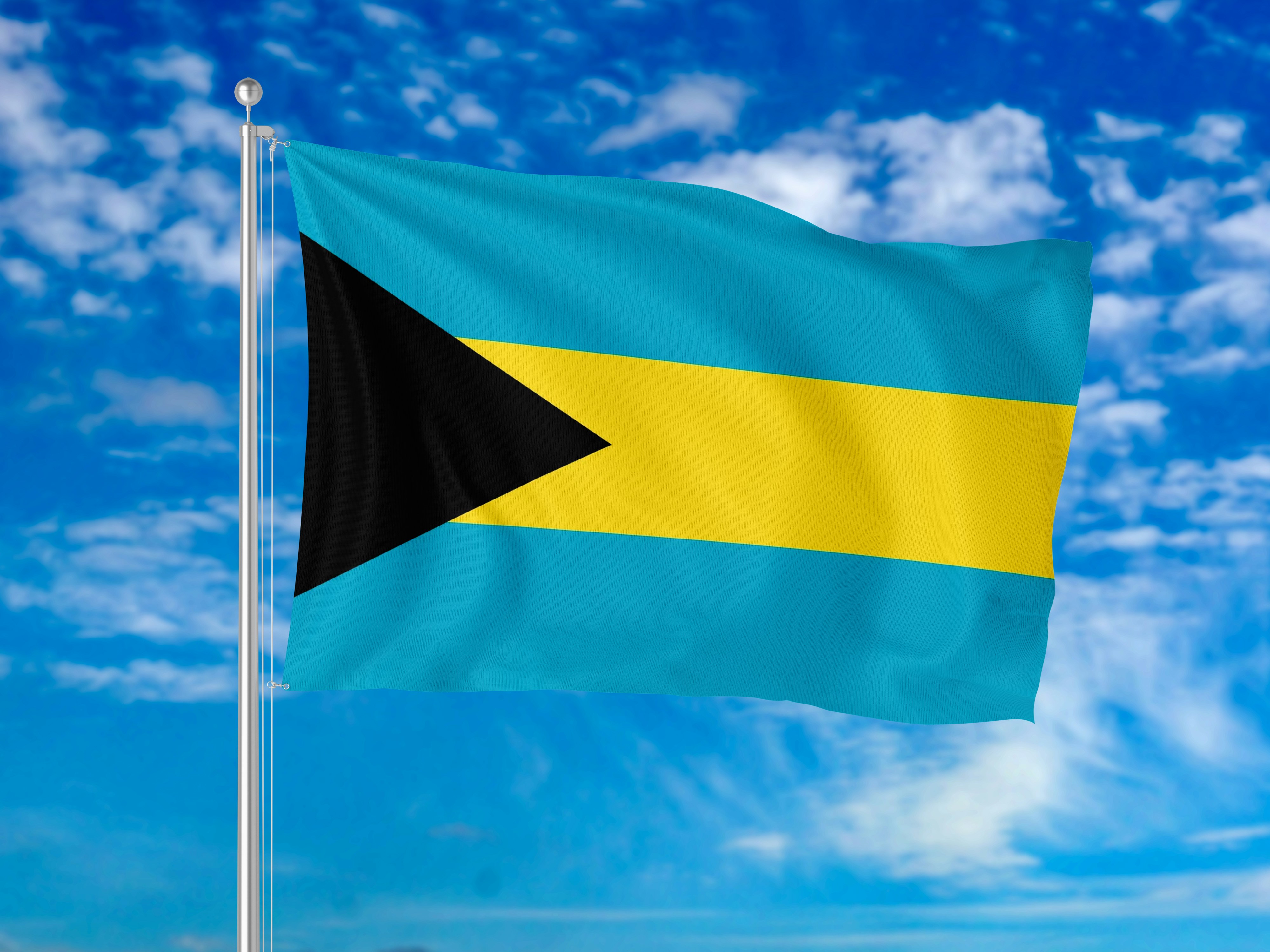 The flag of the Bahamas waving on a pole against a blue sky