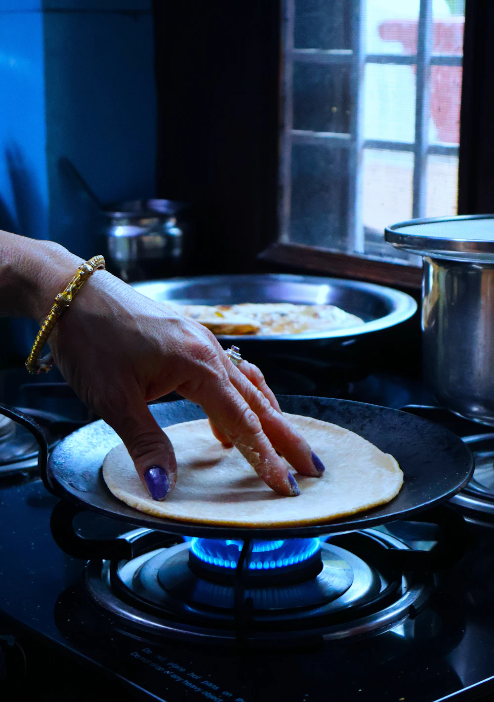 A hand with a gold bangle laying a dosa on a hot tawa