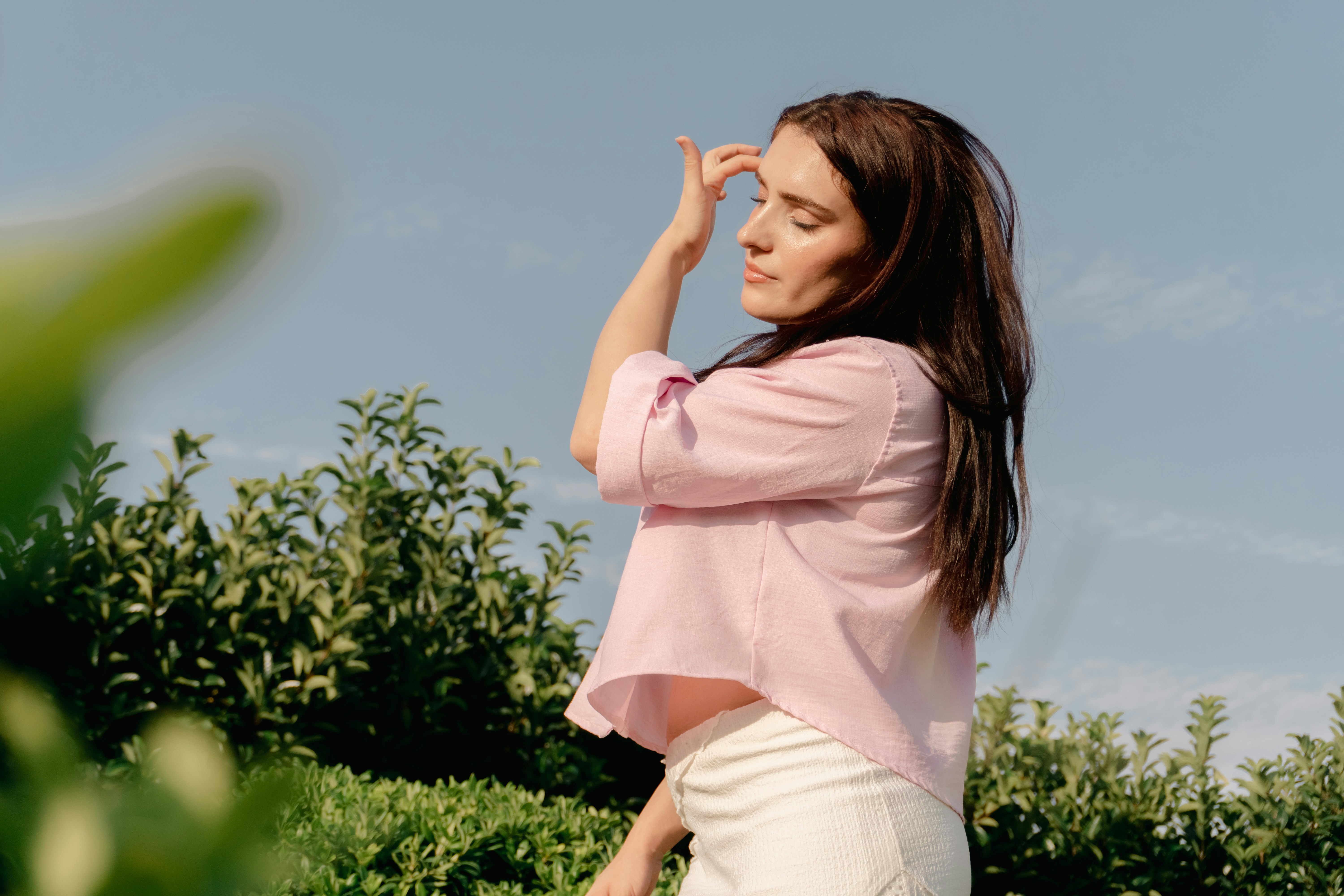 A woman in a pink shirt touching her hair outdoors against a blue sky