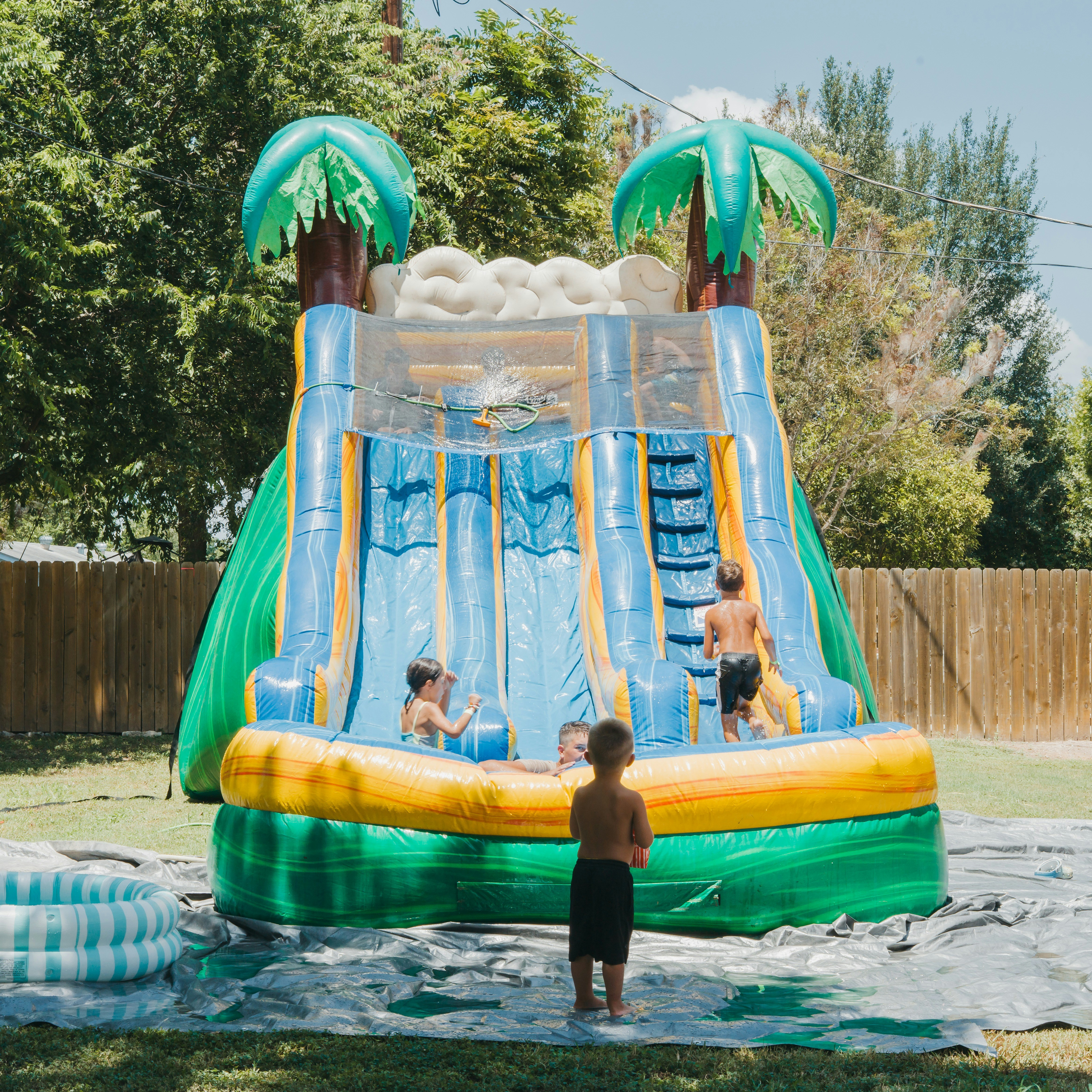 Children playing on a large inflatable water slide in a sunny backyard