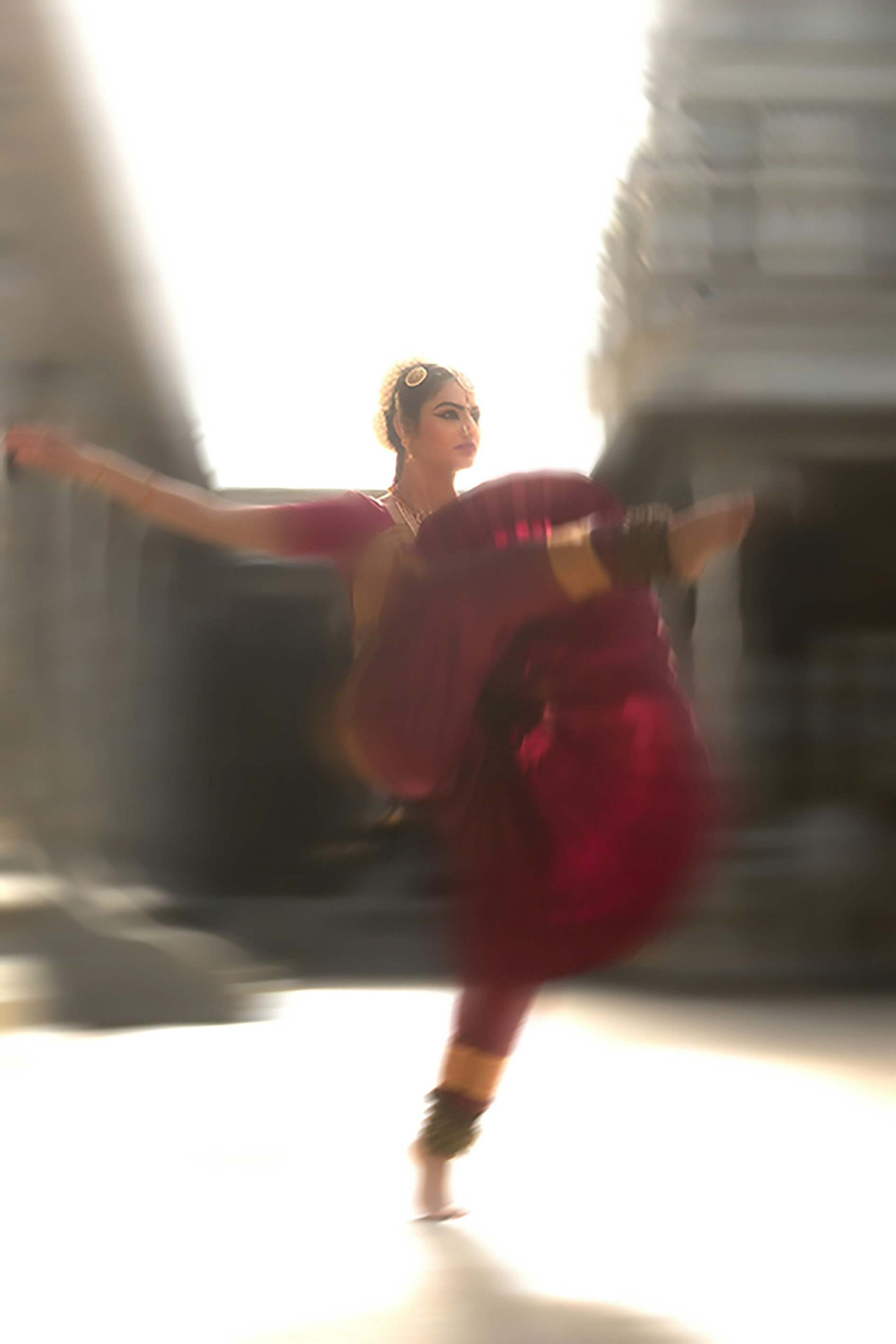 A woman in a maroon sari performing a traditional dance with motion blur