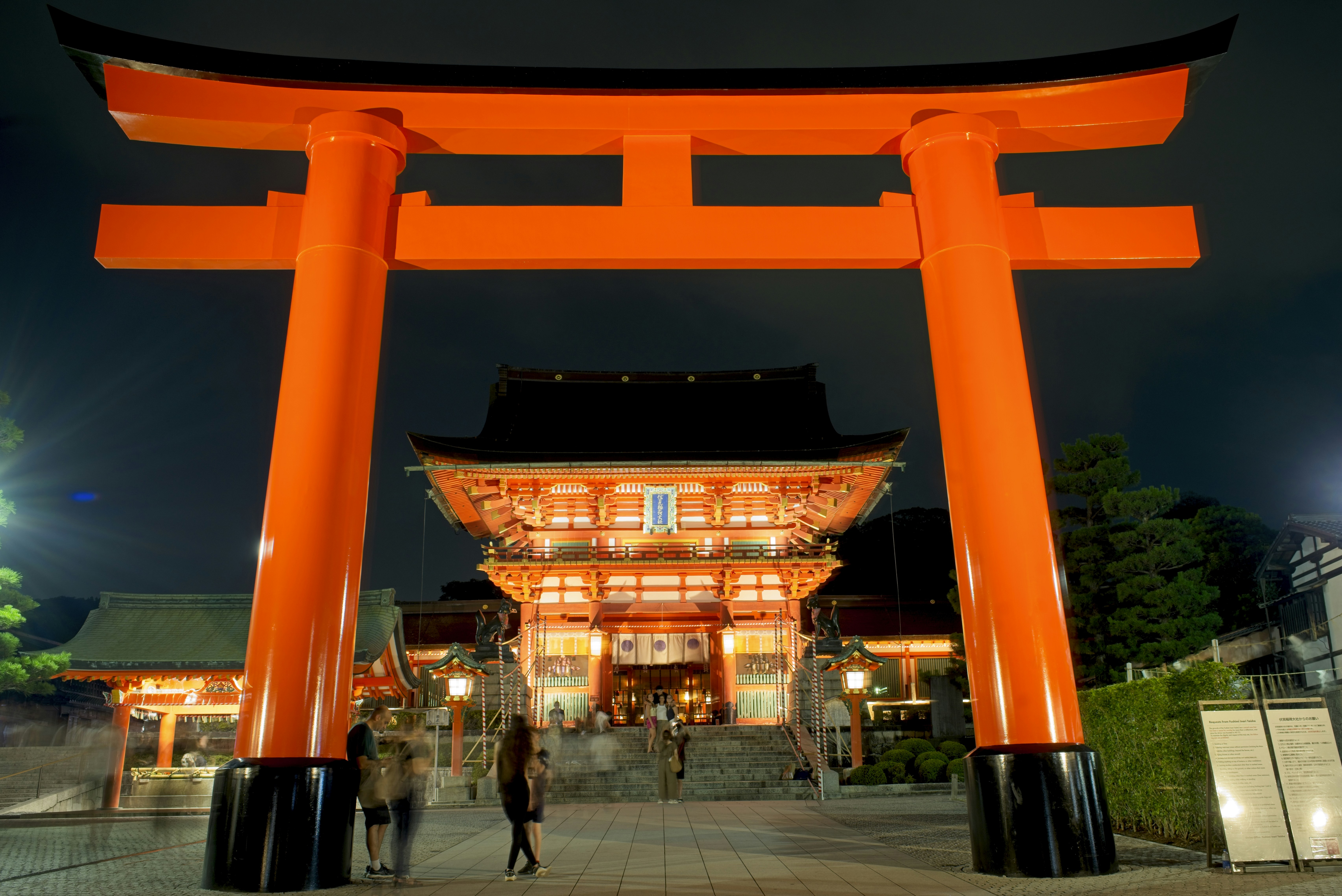 Una gran puerta torii naranja en la entrada de un santuario japonés muy iluminado.