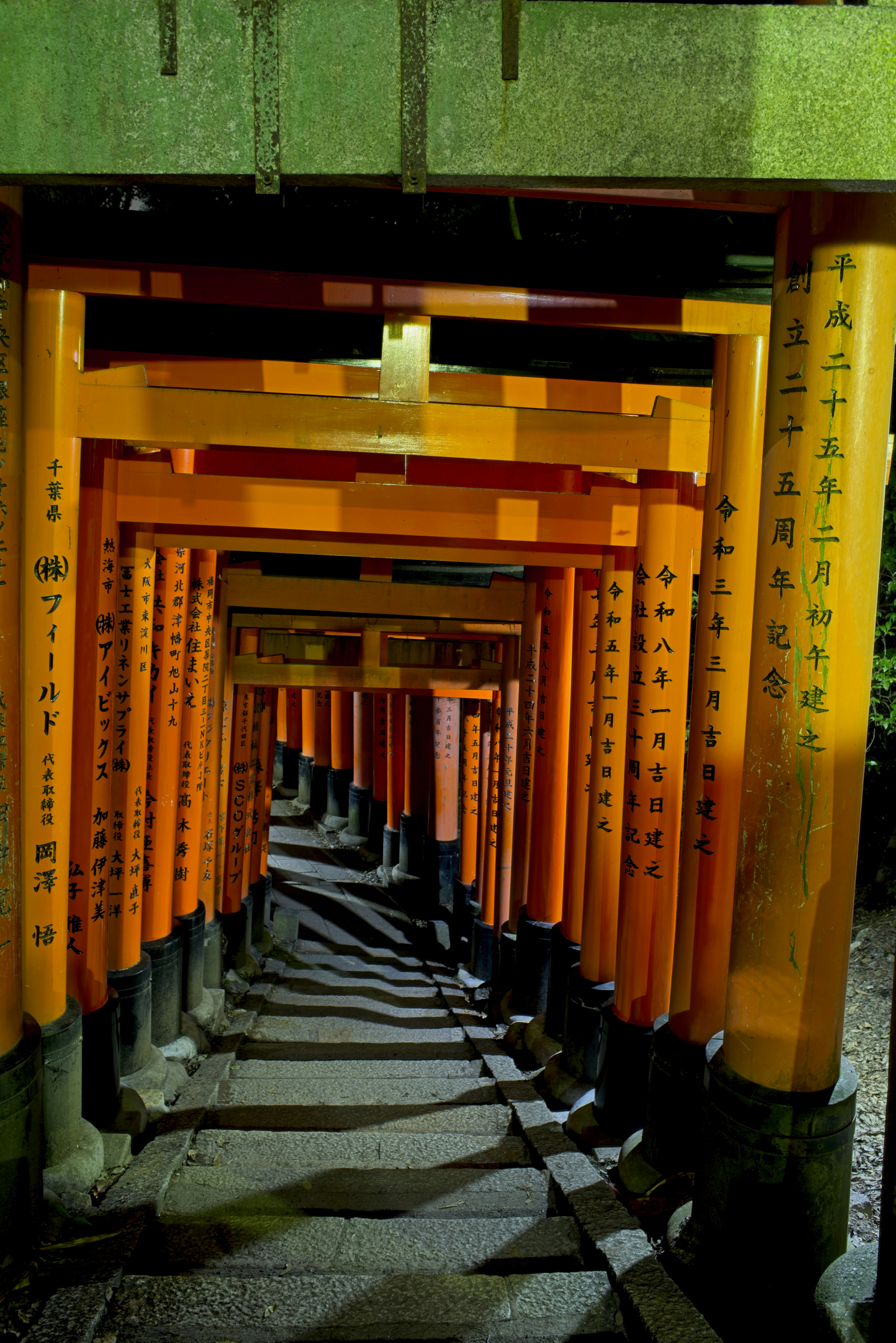 Una escalera de piedra que desciende por un túnel de torii naranjas por la noche.