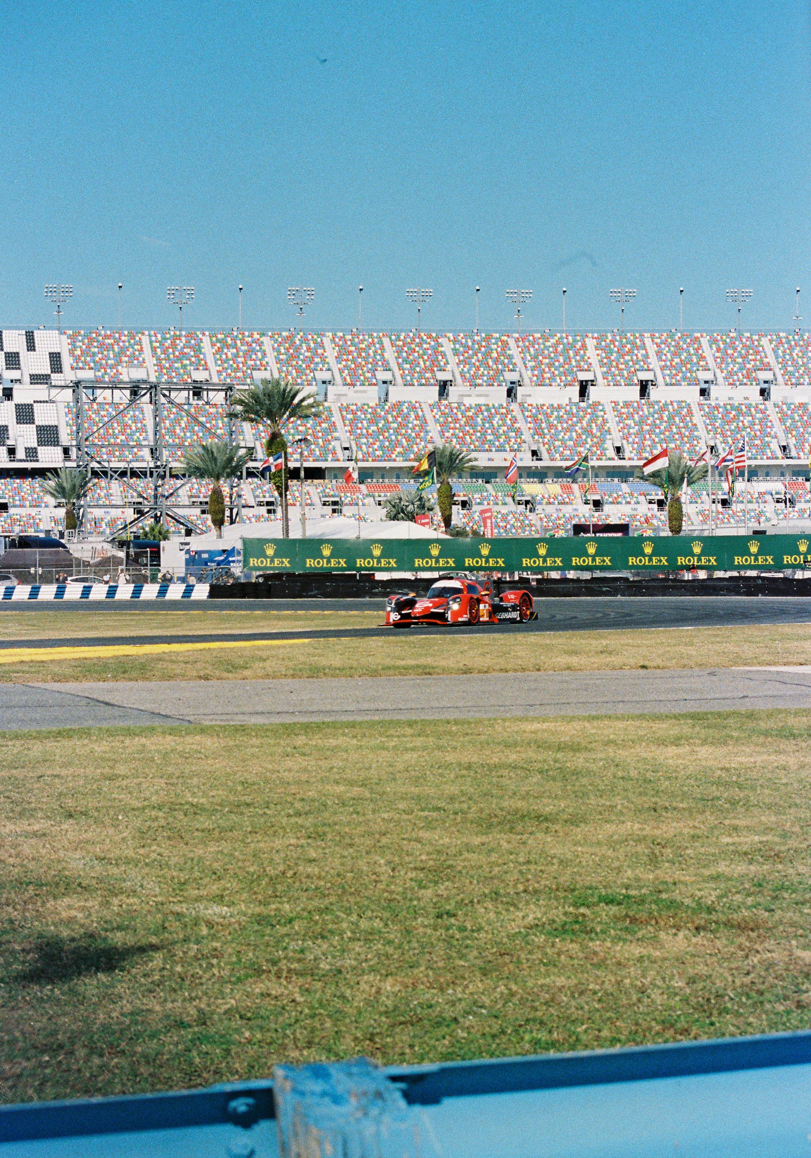 A red race car driving on a track in front of large stadium seating.