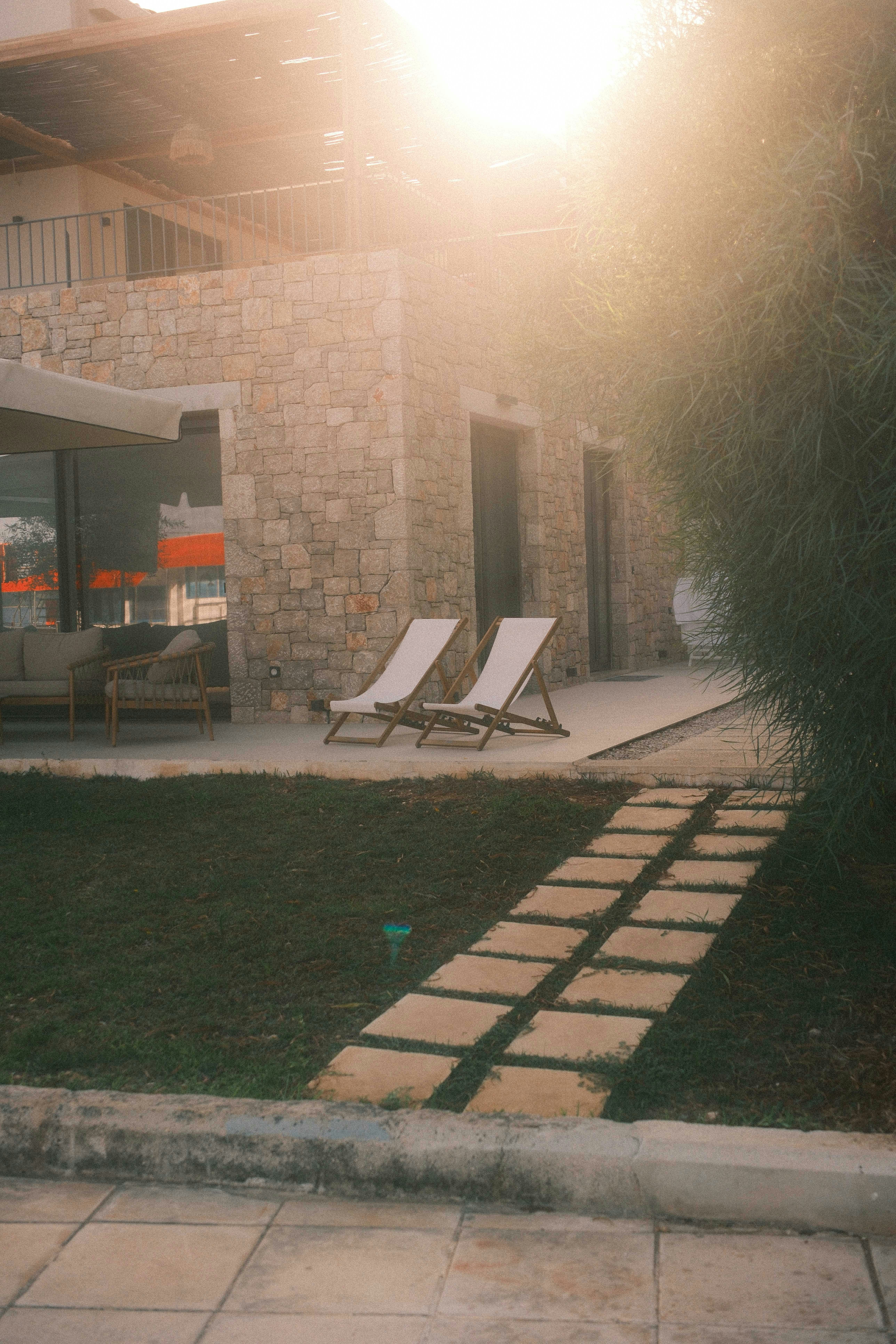 Two lounge chairs on a stone patio in warm, low evening light