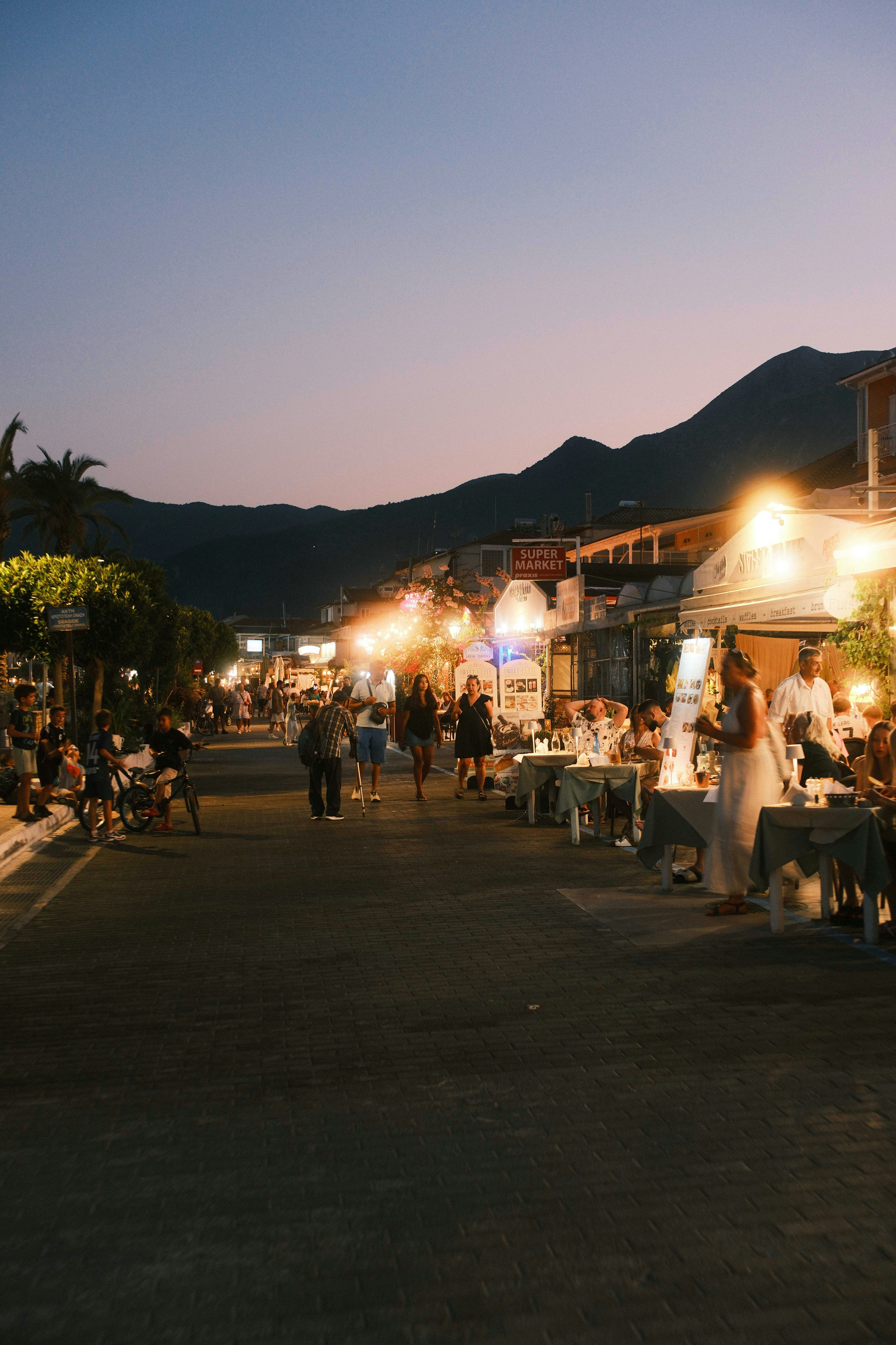 People walking along a street lined with restaurants and shops at dusk