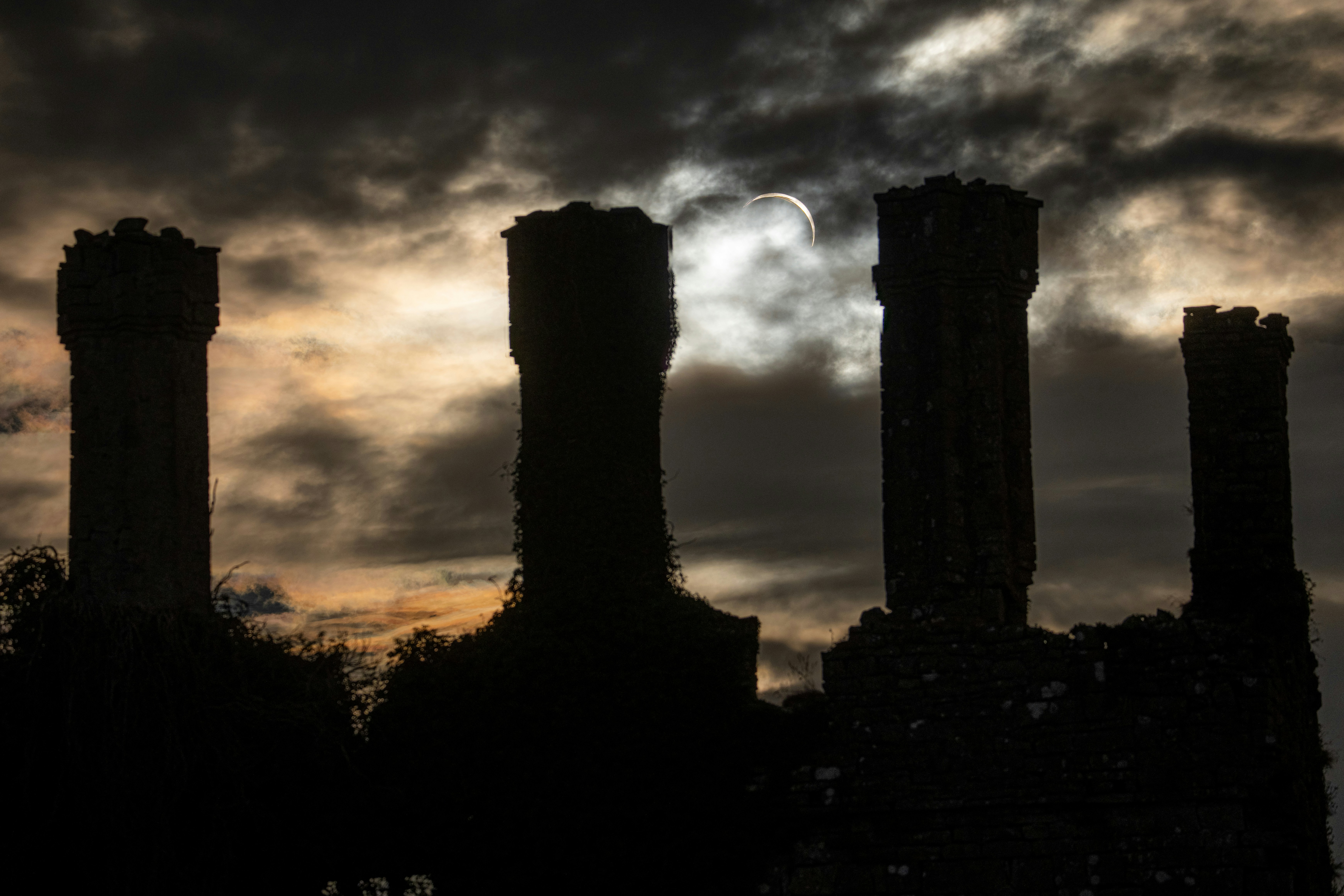 Four stone chimneys in silhouette against a cloudy sky with a partial solar eclipse