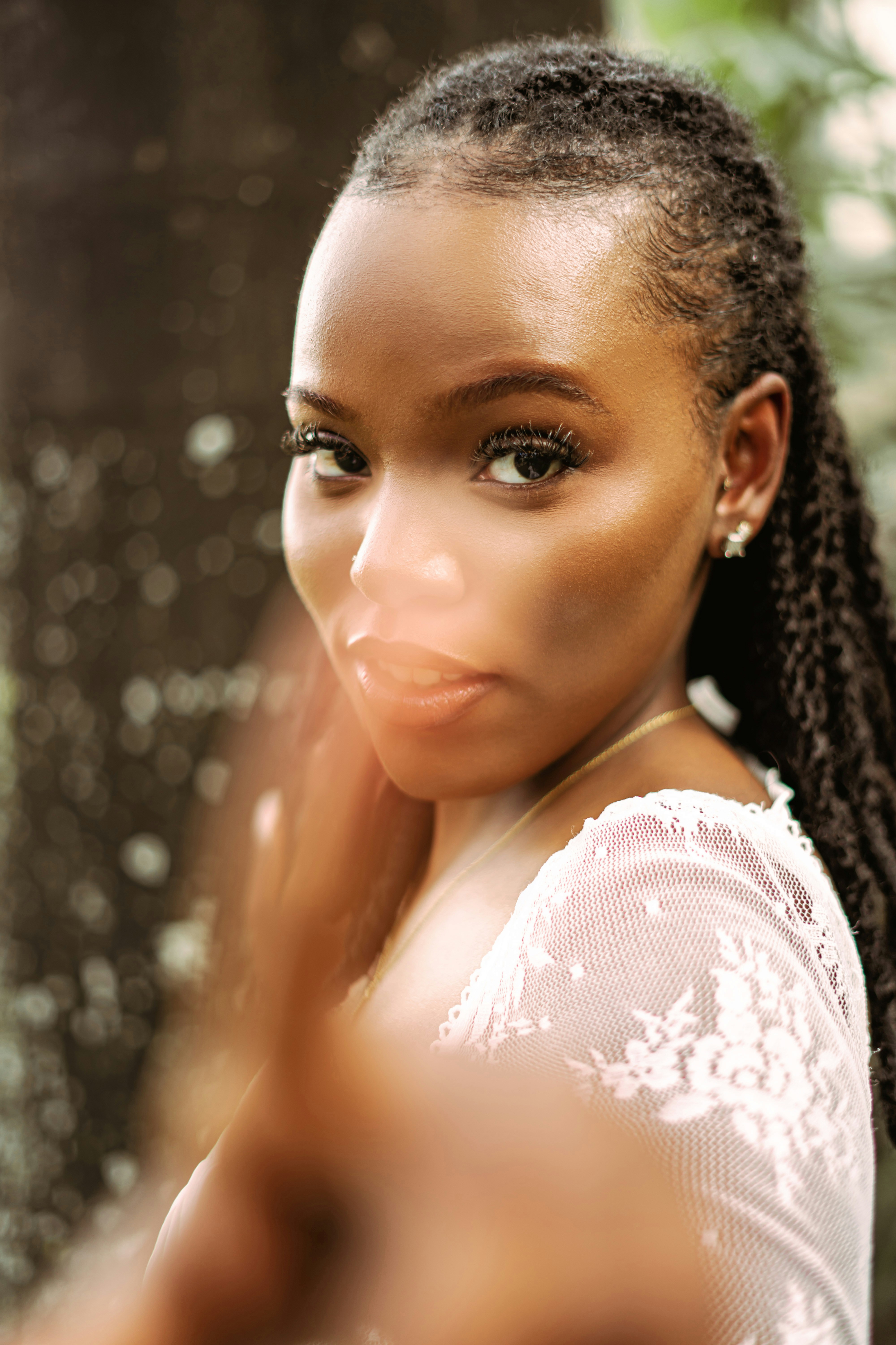 A woman with braided hair in a white lace top looking at the camera