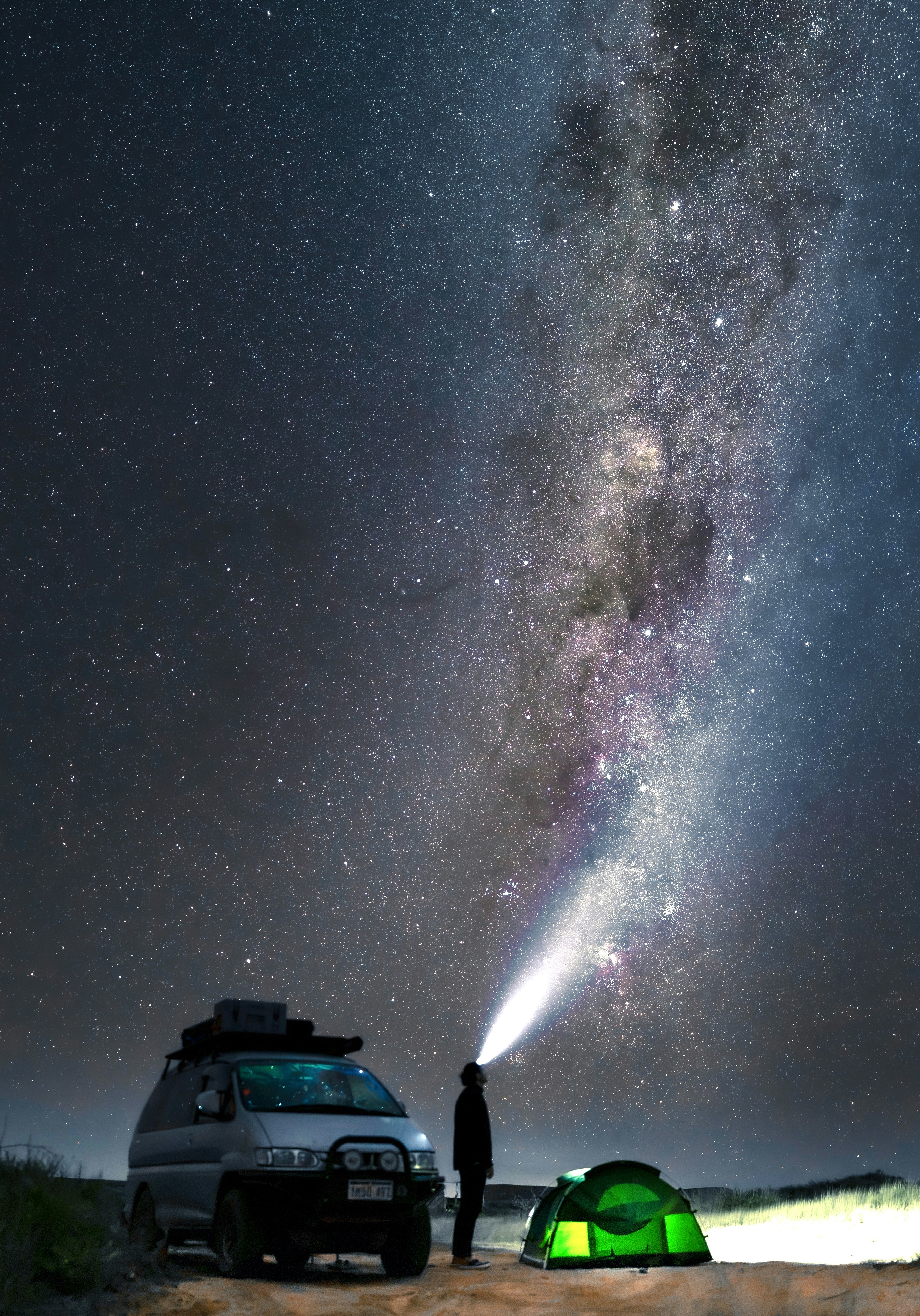 Une personne avec un faisceau de lampe frontale pointant vers la galaxie de la Voie lactée la nuit
