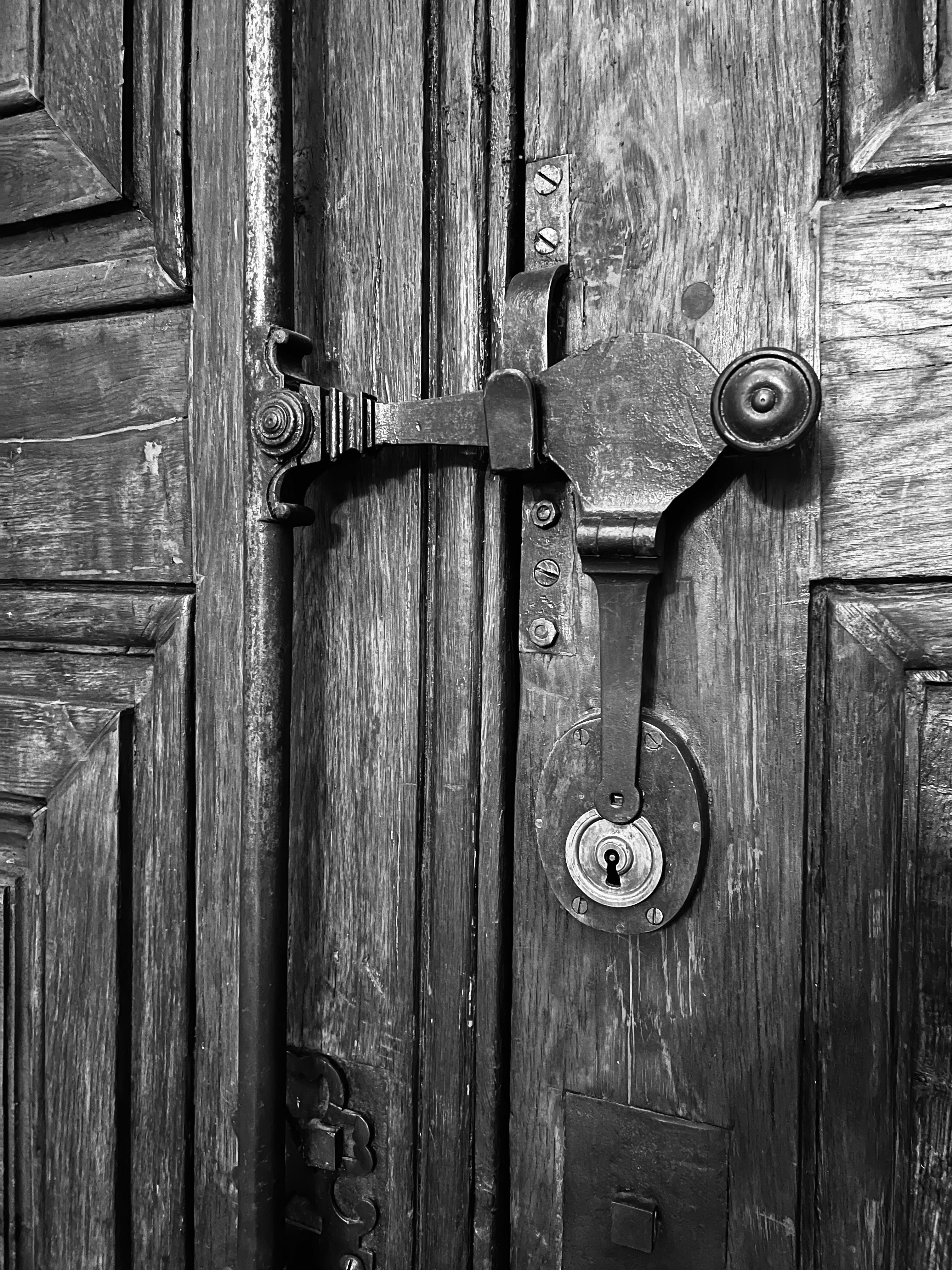 An ornate metal latch and keyhole on a weathered wooden door
