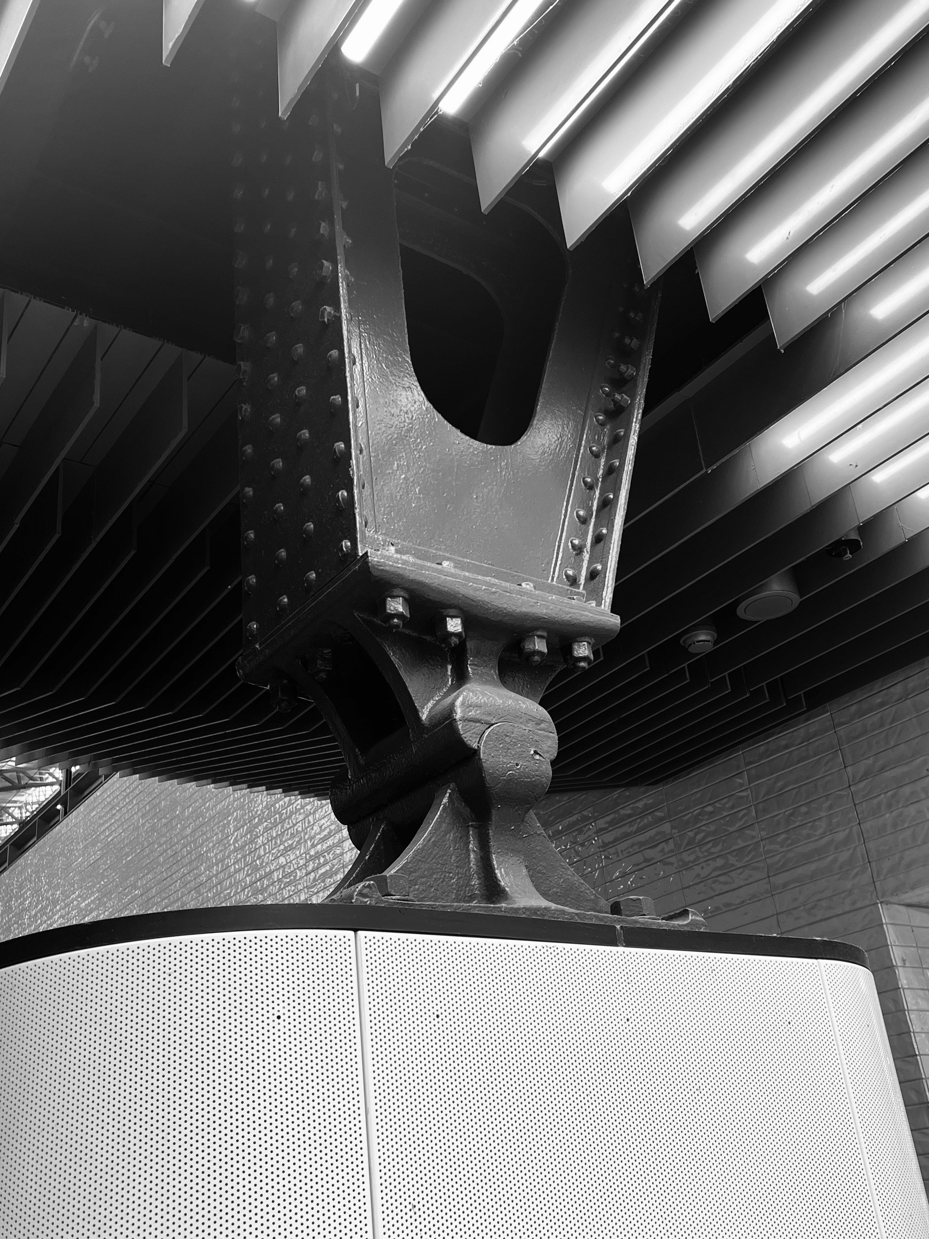 A black and white view of a riveted steel support column under a ceiling