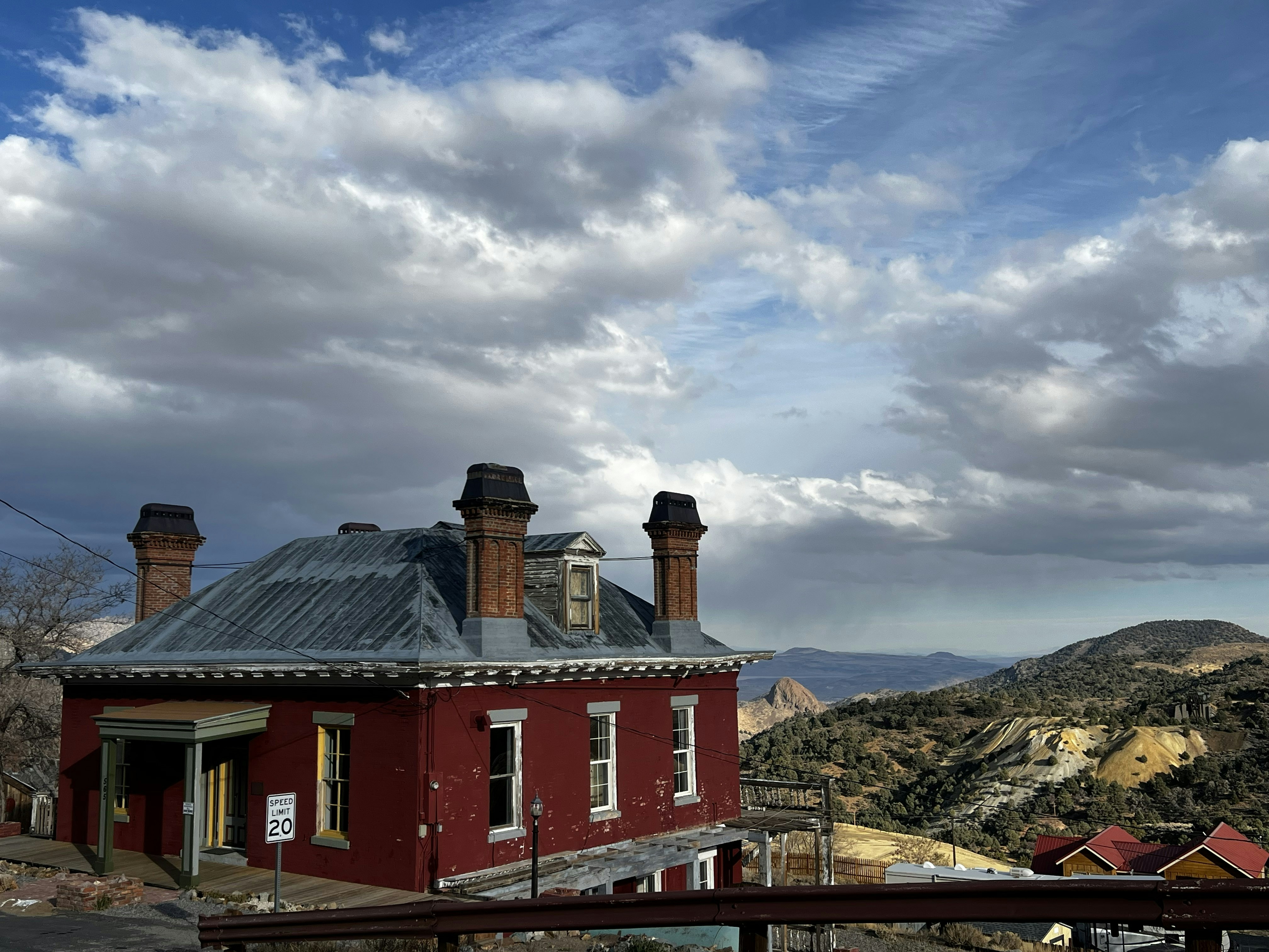 A red historic building with three chimneys overlooking a rugged mountain landscape under clouds