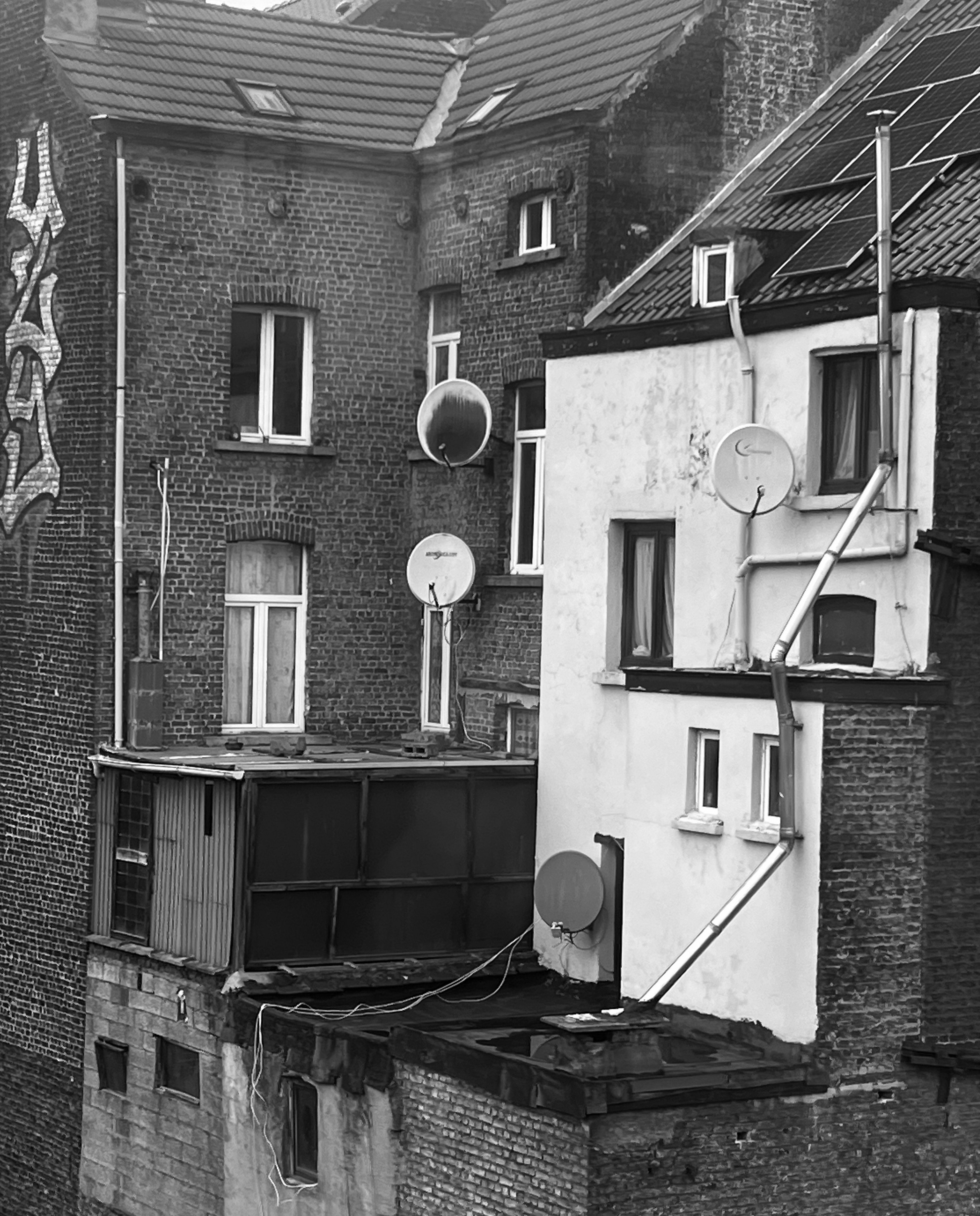 Black and white view of brick buildings with satellite dishes and rooftop solar panels