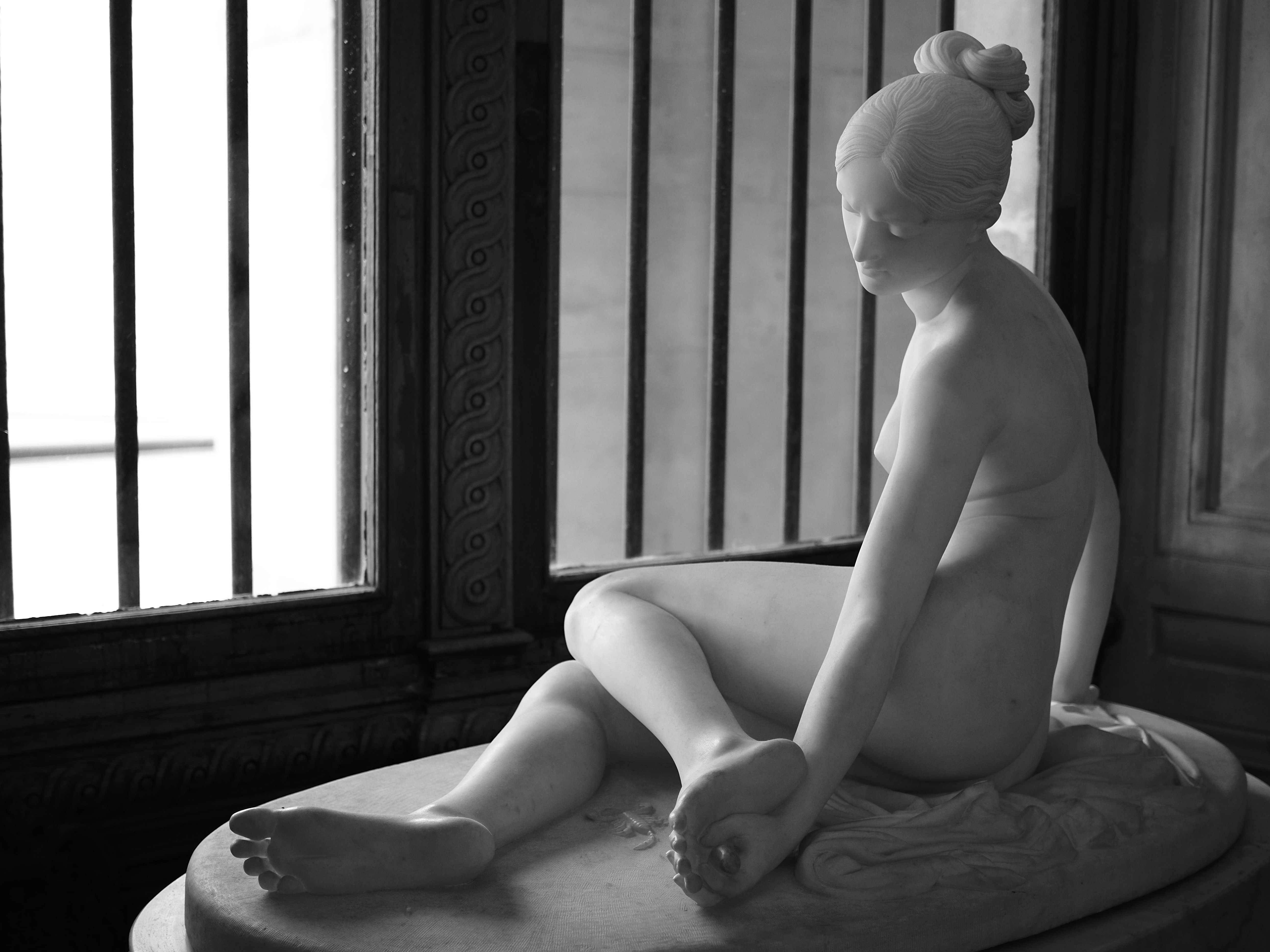 A white marble sculpture of a seated woman with hair in a bun