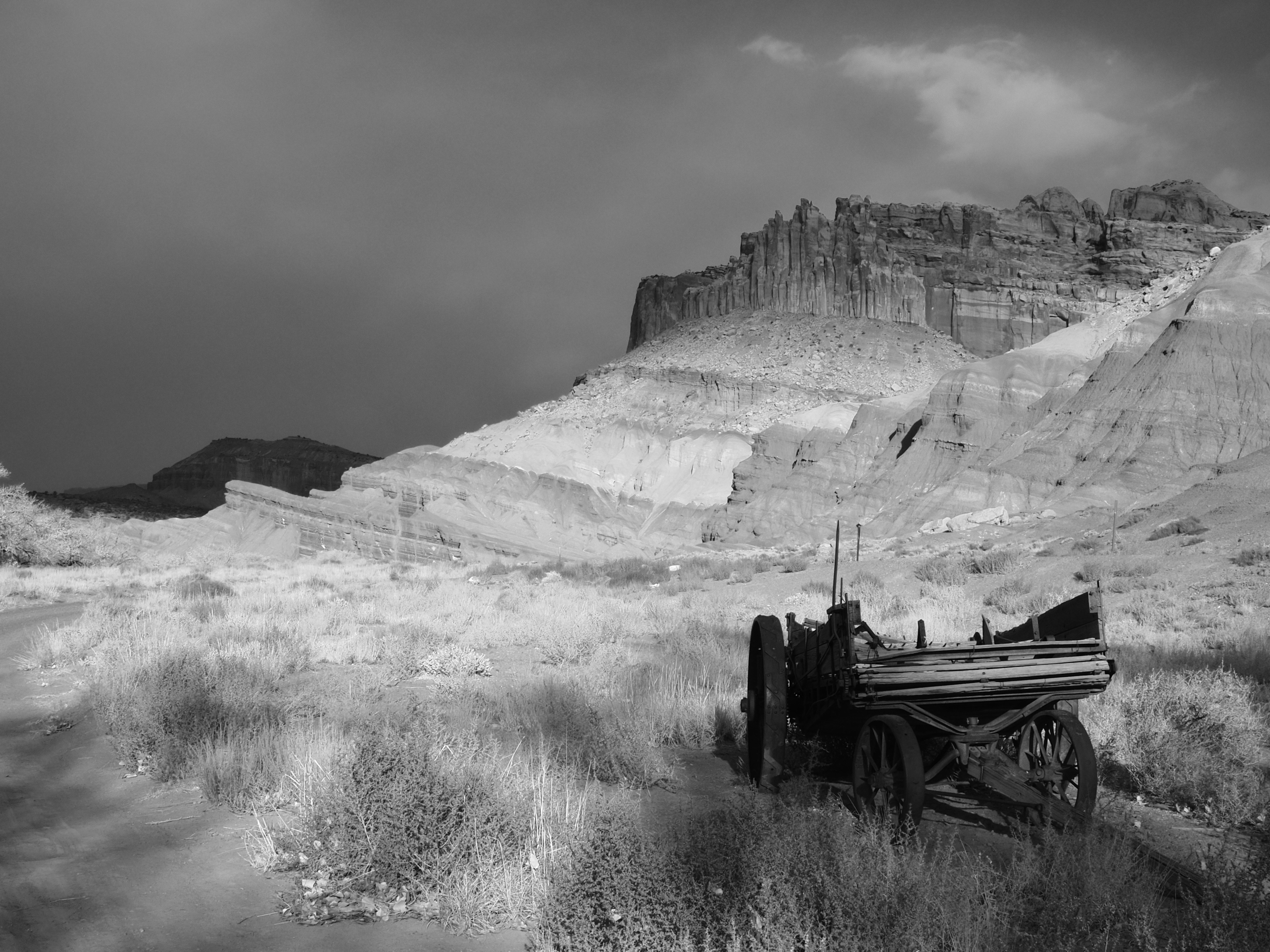 An old wooden wagon in a desert landscape with rocky cliffs under dark clouds
