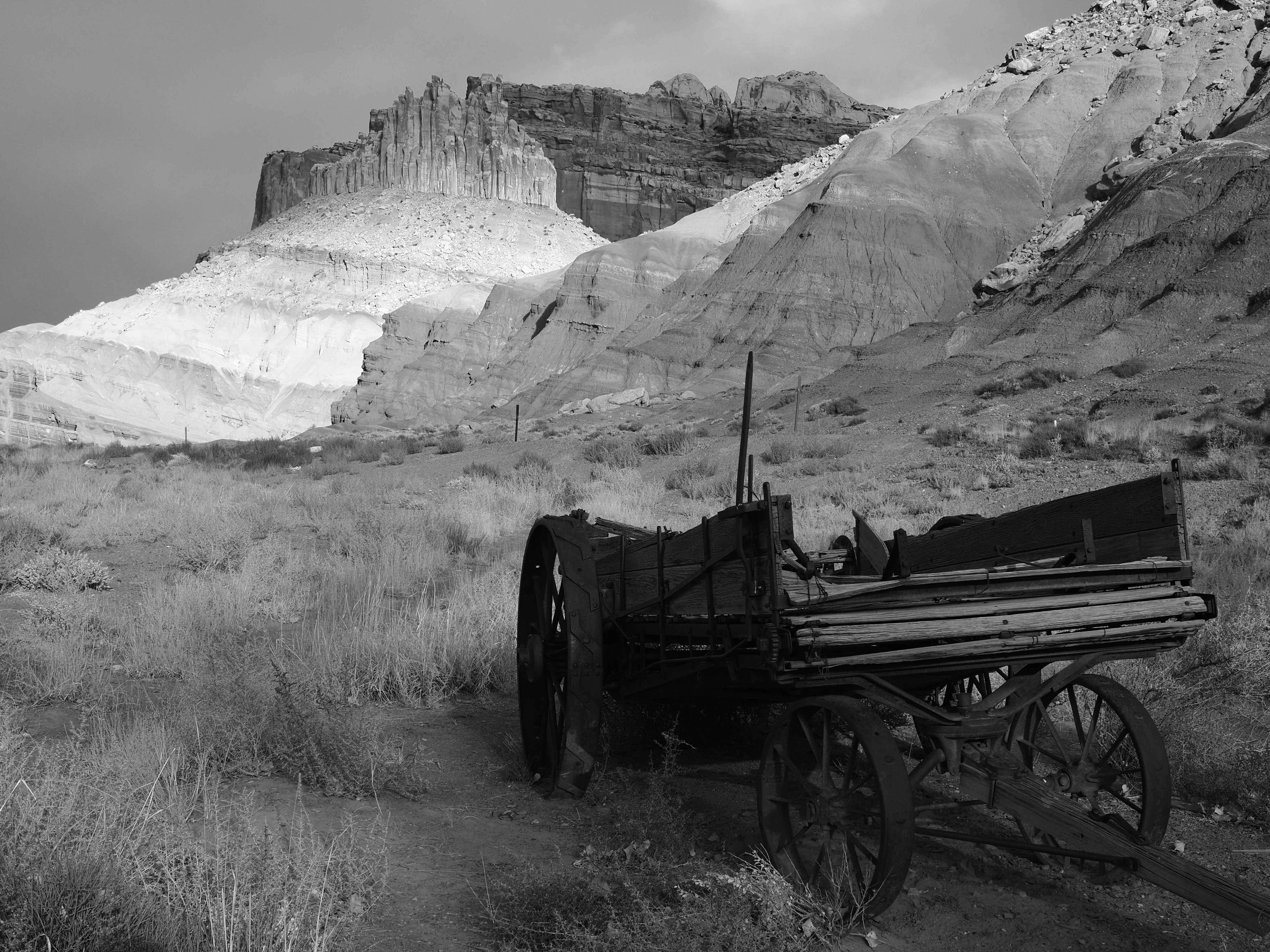 An old wooden wagon in a desert landscape with rocky cliffs in the background